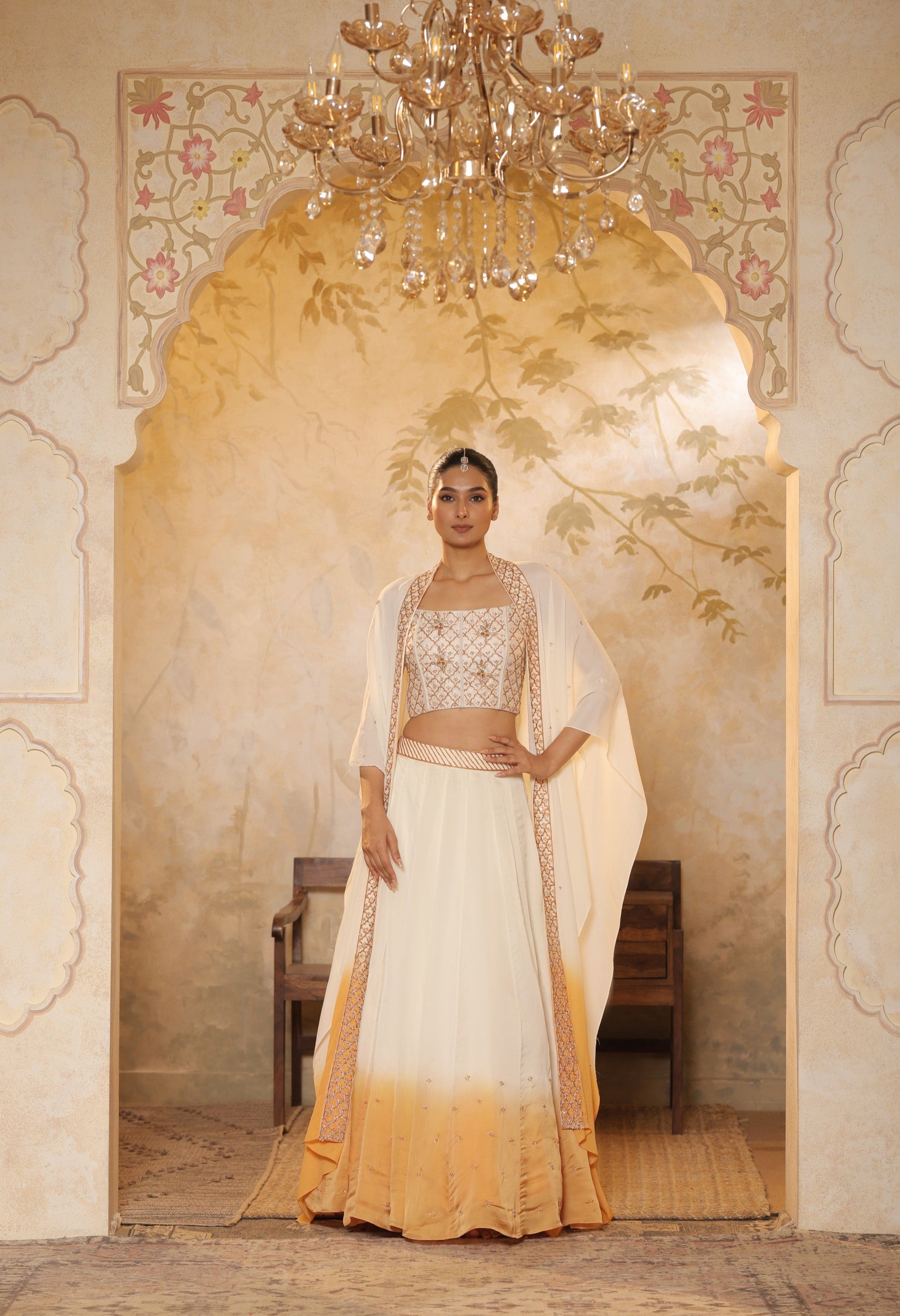 Woman in a traditional outfit standing in an ornate doorway with a chandelier above.