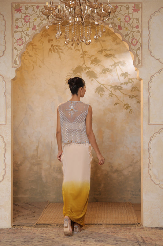 Woman in a stylish outfit standing in an ornate room with a chandelier. Ivory yellow draped skirt set, handcrafted crepe outfit, luxury evening wear, elegant festive attire, designer ethnic ensemble, Sunanta Madaan, near me, Mumbai, Delhi, Hyderabad, Bangalore, Pune