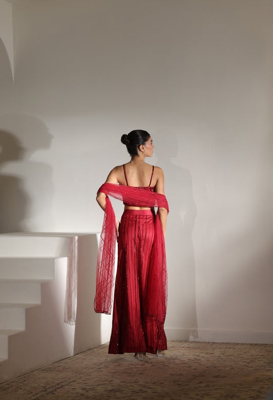 Woman in a red outfit holding a matching scarf against a white wall. Sunanta Madaan – Burgundy Satin Embroidered Western Skirt Set, Handcrafted Festive Wear, Elegant Party Outfit, Boho Indo-Western Dress, Indo-Western Fusion Wear, Indo-Western Attire for Engagement, Indo-Western Outfit for Sangeet, Indo-Western Draped & Embroidered Skirt, Women’s Designer Festive Ensemble, Mumbai, Jaipur, Hyderabad, Ahmedabad, Pune, near me
