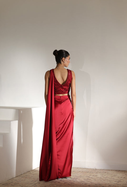 Woman in a red saree standing against a plain white wall; Sunanta Madaan – Maroon Satin Embroidered Draped Saree, Elegant Wedding Wear, Premium Festive Outfit, Boho Indo-Western Dress, Indo-Western Fusion Wear, Indo-Western Attire for Engagement, Indo-Western Outfit for Sangeet, Indo-Western Draped & Embroidered Saree, Women’s Designer Bridal Ensemble, Delhi, Jaipur, Hyderabad, Ahmedabad, Bangalore, near me