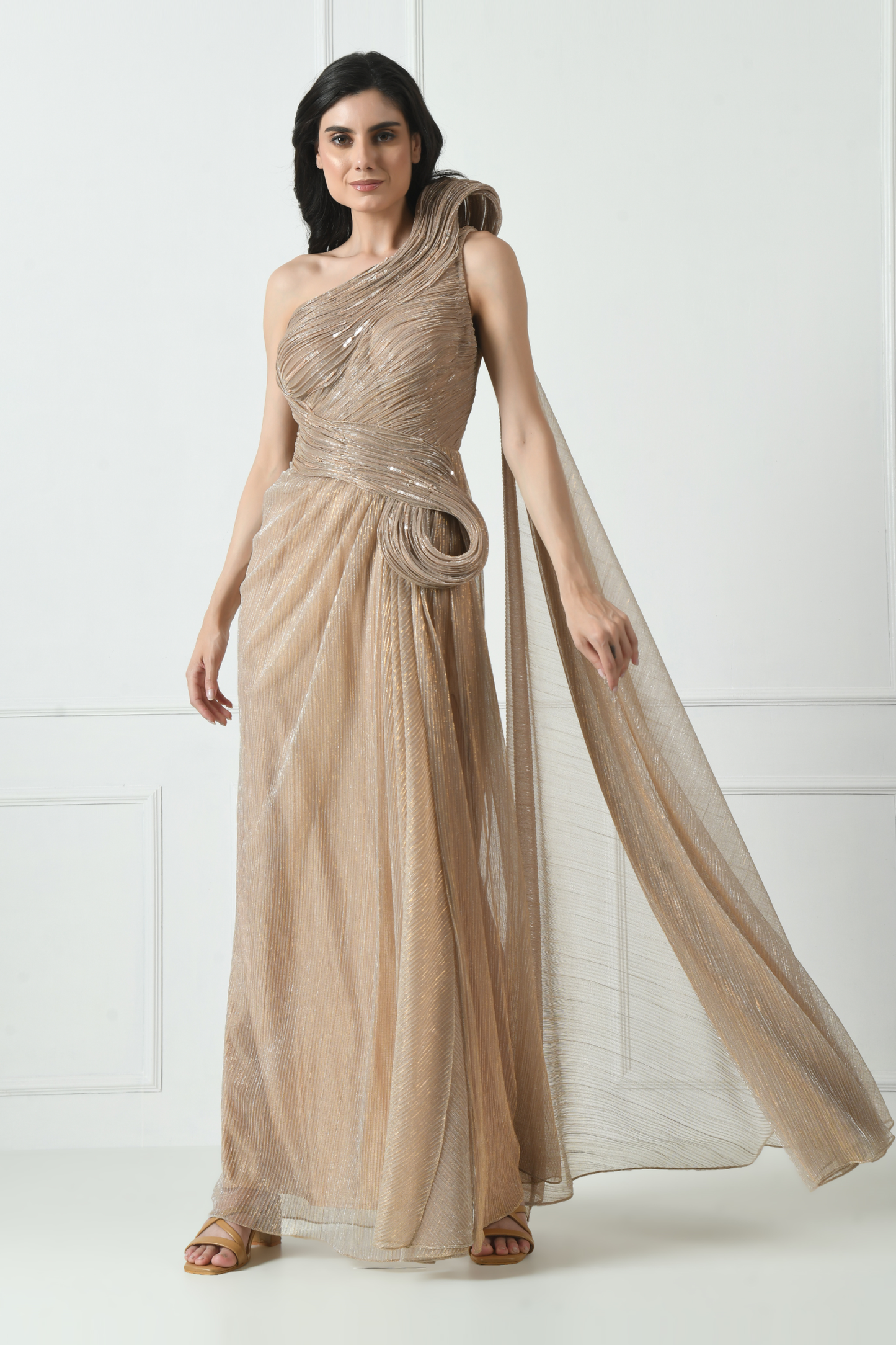 A woman wearing a golden cocktail gown with structured detailing, standing in a room with white panelled walls. Sunanta Madaan – Golden Cocktail Gown for Women, Structured Evening Dress, Elegant Party Wear, Indo-Western Fusion Gown, Women’s Formal Dress, Indo-Western Attire for Reception, Party Outfit, Boho Indo-Western Dress, Indo-Western Draped Dress, Mumbai, Delhi, Hyderabad, Bangalore, Pune, near me