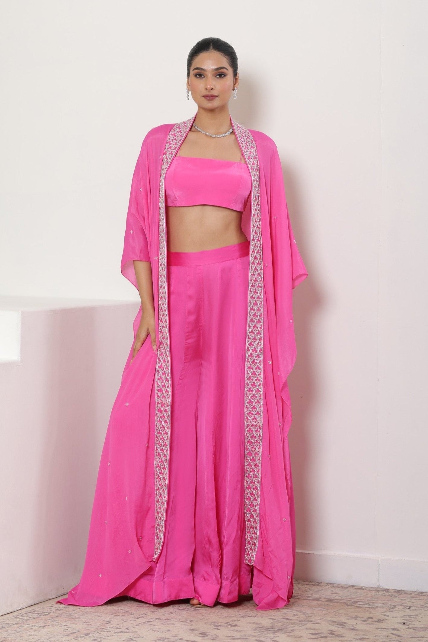 Woman wearing a pink traditional outfit with a white background; Hot pink sharara set, embroidered crepe outfit, handcrafted evening wear, elegant festive attire, designer party ensemble, Sunanta Madaan