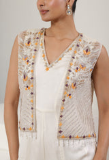 Woman wearing a white embroidered vest with orange and purple details on a plain background; Ivory orange jumpsuit, satin organza outfit, designer cape jumpsuit, elegant occasional wear, festive ethnic attire, Sunanta Madaan, near me, Mumbai, Delhi, Hyderabad, Bangalore, Pune
