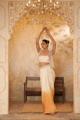 Woman in a traditional outfit standing in a decorated room with a chandelier. Ivory orange skirt dress, hand embroidered crepe outfit, elegant festive wear, designer ethnic attire, premium traditional ensemble, Sunanta Madaan, near me, Mumbai, Delhi, Hyderabad, Bangalore, Pune