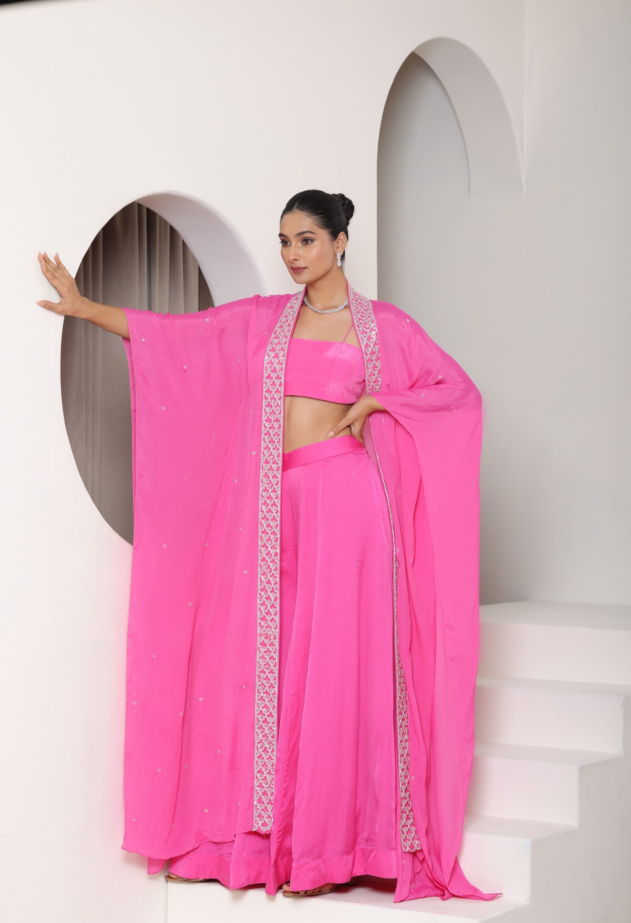 Woman in a bright pink traditional outfit with a flowing drape against a white background; Hot pink sharara set, embroidered crepe outfit, handcrafted evening wear, elegant festive attire, designer party ensemble, Sunanta Madaan