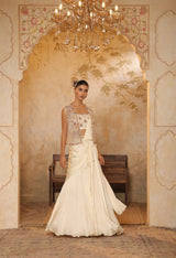 Woman in a traditional outfit standing in an ornate room with a chandelier. ivory georgette saree, saree with embroidered cape, designer wedding saree India, Indo Western bridal outfit, elegant ivory saree, Sunanta Madaan