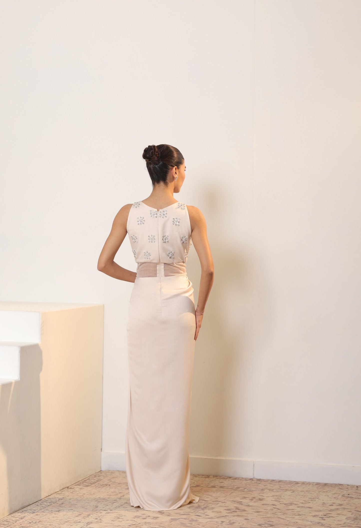 Woman wearing a white dress with lace details in a minimal indoor setting; Sunanta Madaan – Ivory Crepe Satin Western Embroidered Gown, Premium Cocktail Wear, Elegant Party Outfit, Boho Indo-Western Dress, Indo-Western Fusion Wear, Women’s Formal Evening Dress, Indo-Western Outfit for Reception, Party Outfit, Indo-Western Draped Dress, Jaipur, Delhi, Hyderabad, Ahmedabad, Bangalore, near me