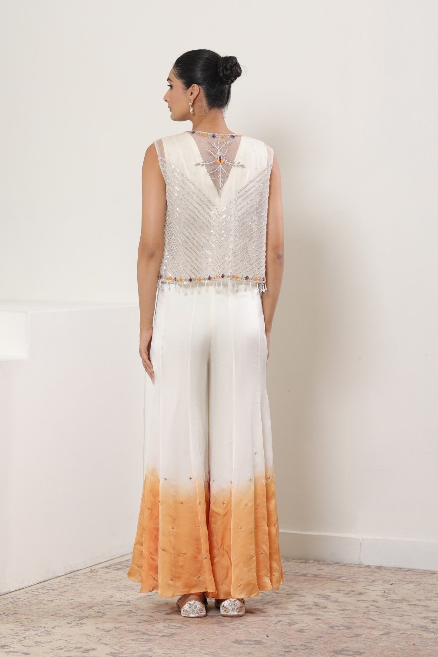 Woman wearing a sleeveless top and wide-leg pants with a gradient design against a white background; Ivory orange jumpsuit, satin organza outfit, designer cape jumpsuit, elegant occasional wear, festive ethnic attire, Sunanta Madaan, near me, Mumbai, Delhi, Hyderabad, Bangalore, Pune