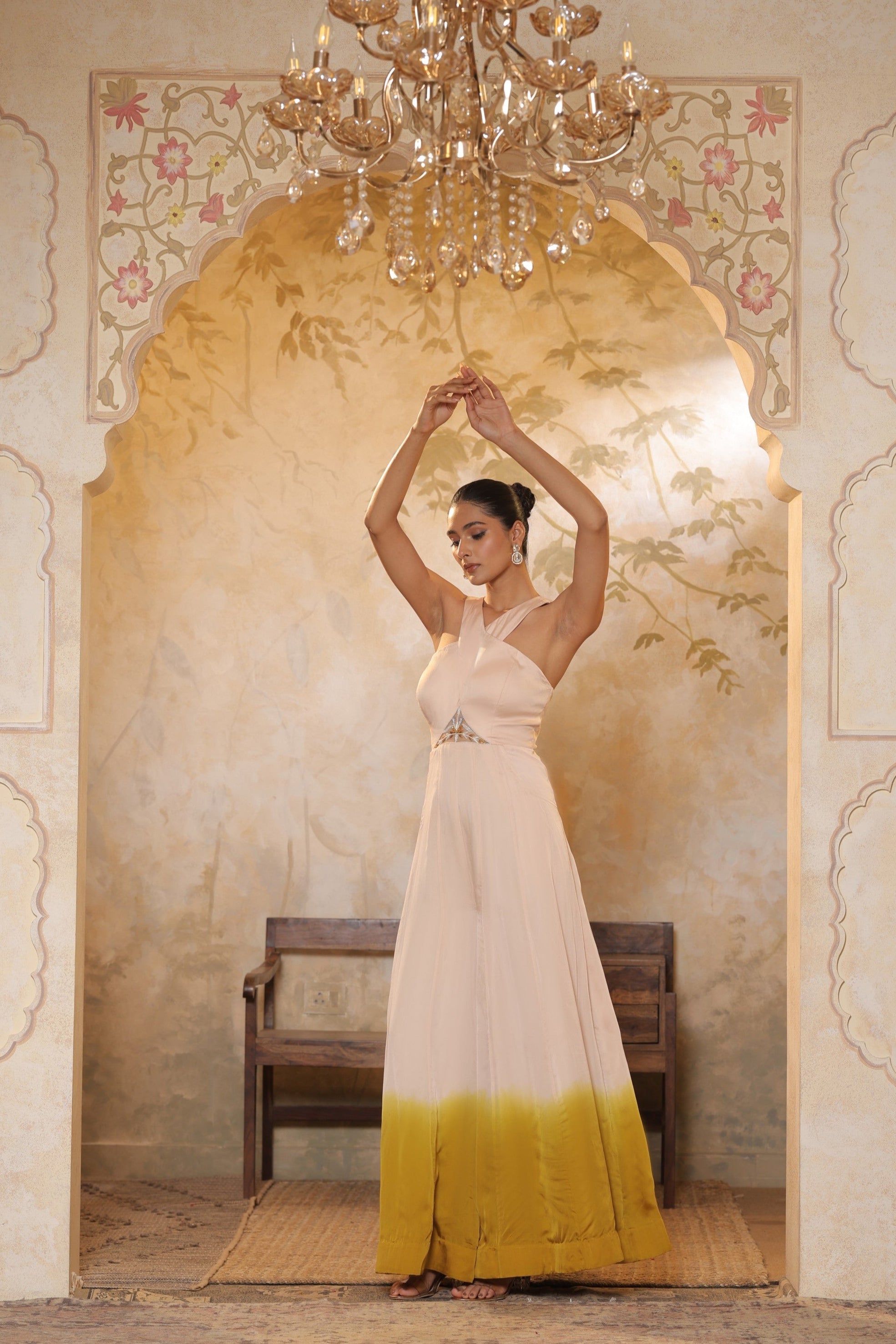 Woman in a white and yellow dress standing in a decorated room with a chandelier. Ivory yellow jumpsuit, satin organza outfit, Sunanta Madaan, sequin work haldi wear, premium festive attire, elegant designer jumpsuit, Mumbai, Delhi, Hyderabad, Bangalore, Pune, Jaipur, Lucknow, Near Me