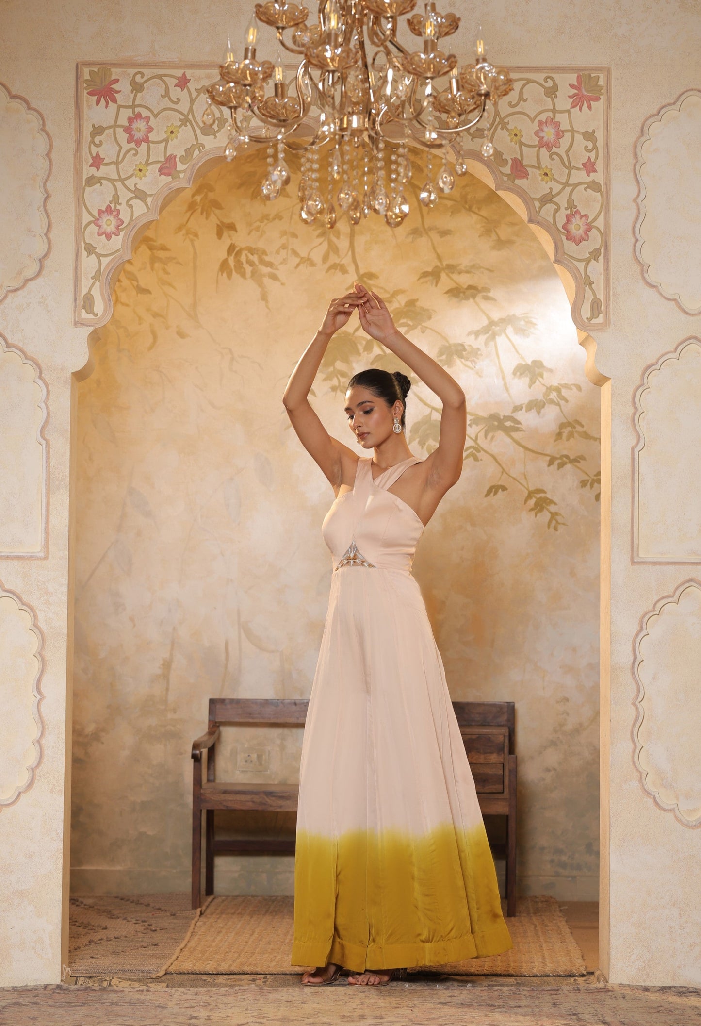 Woman in a white and yellow dress standing in a decorated room with a chandelier. Ivory yellow jumpsuit, satin organza outfit, Sunanta Madaan, sequin work haldi wear, premium festive attire, elegant designer jumpsuit, Mumbai, Delhi, Hyderabad, Bangalore, Pune, Jaipur, Lucknow, Near Me