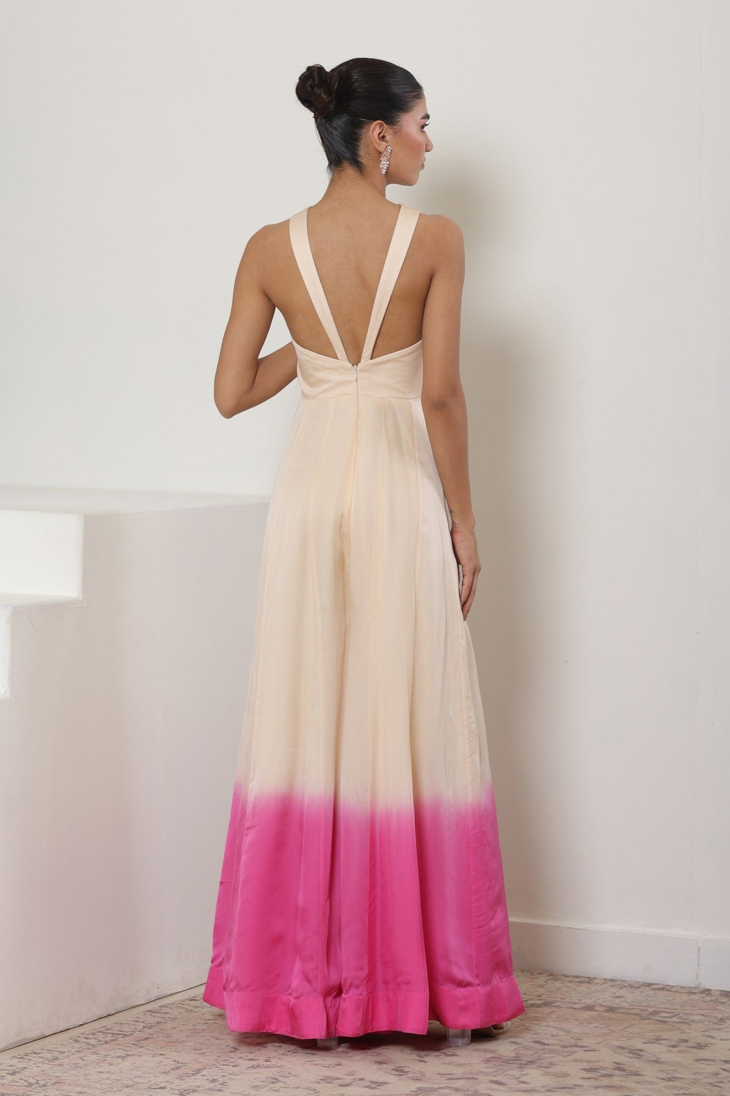 Woman wearing a long, off-white dress with a pink gradient at the bottom against a plain background. Ivory pink jumpsuit, satin organza outfit, embroidered festive wear, elegant designer jumpsuit, premium ethnic attire, Sunanta Madaan, near me, Mumbai, Delhi, Hyderabad, Bangalore, Pune