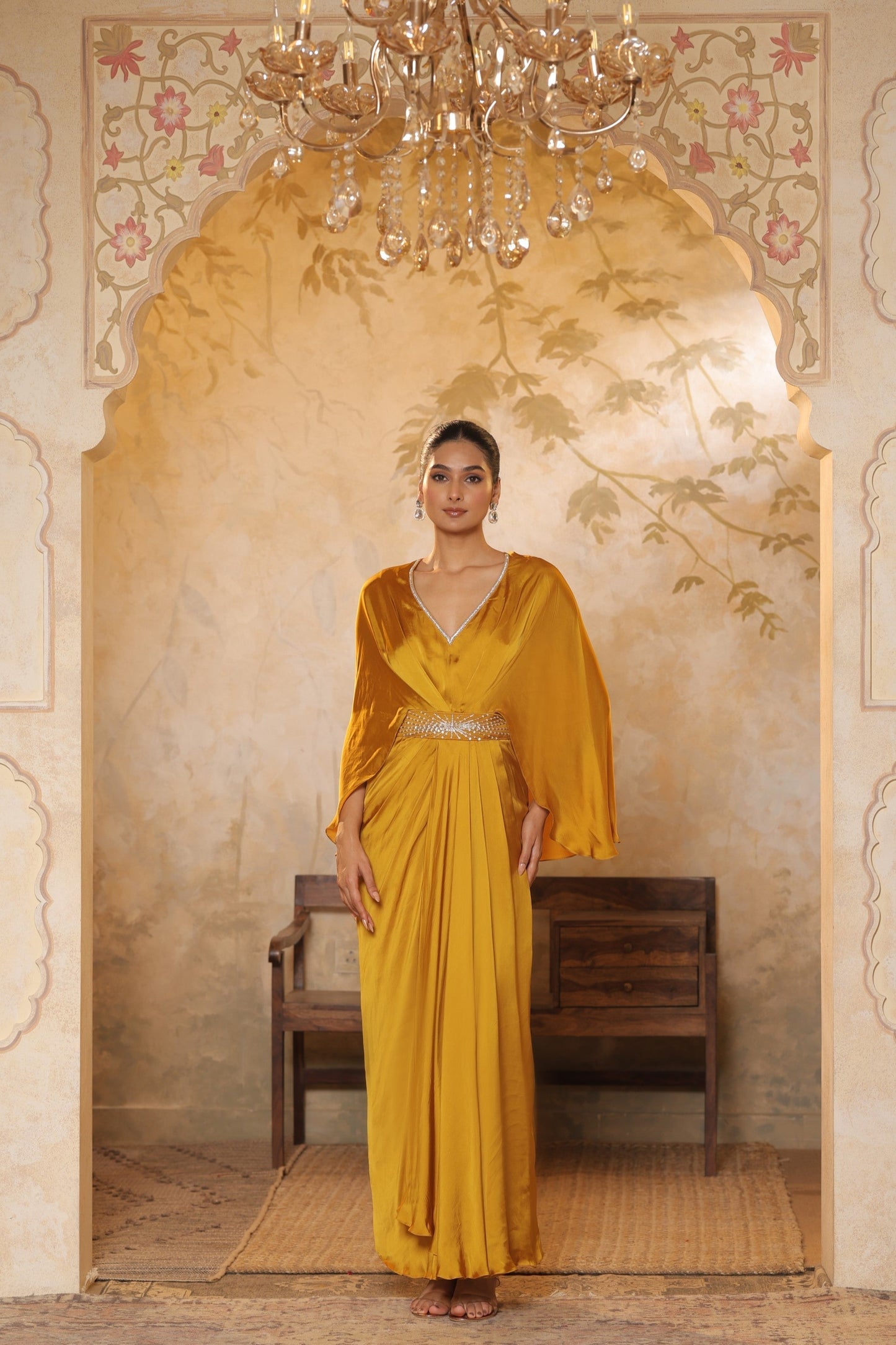 Woman in a yellow dress standing in an ornate room with a chandelier. Yellow crepe kaftan, V-neck embroidered kaftan, handcrafted festive outfit, elegant ethnic wear, designer party kaftan, Sunanta Madaan