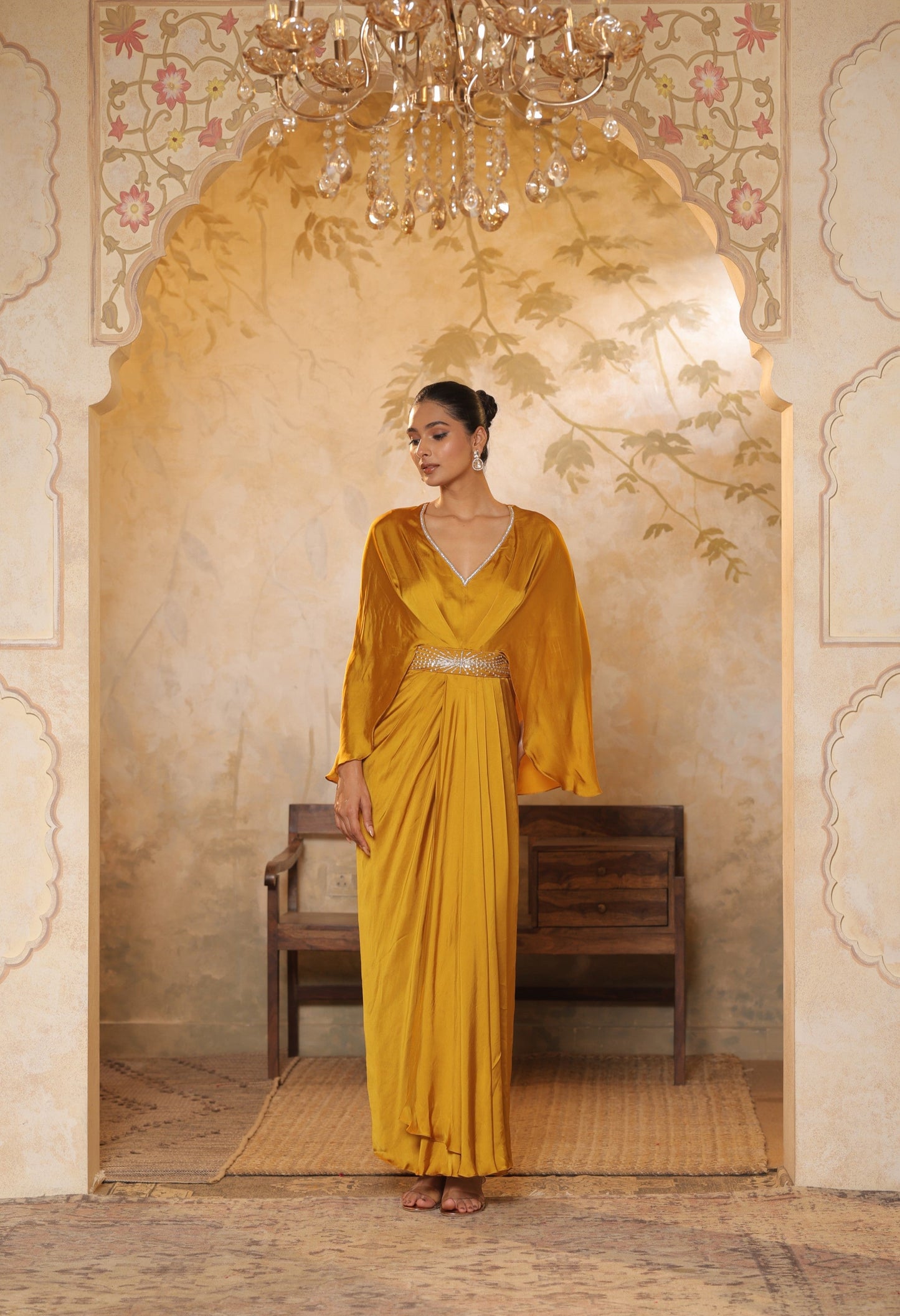 Woman in a yellow saree standing in an ornate room with a chandelier. Yellow crepe kaftan, V-neck embroidered kaftan, handcrafted festive outfit, elegant ethnic wear, designer party kaftan, Sunanta Madaan