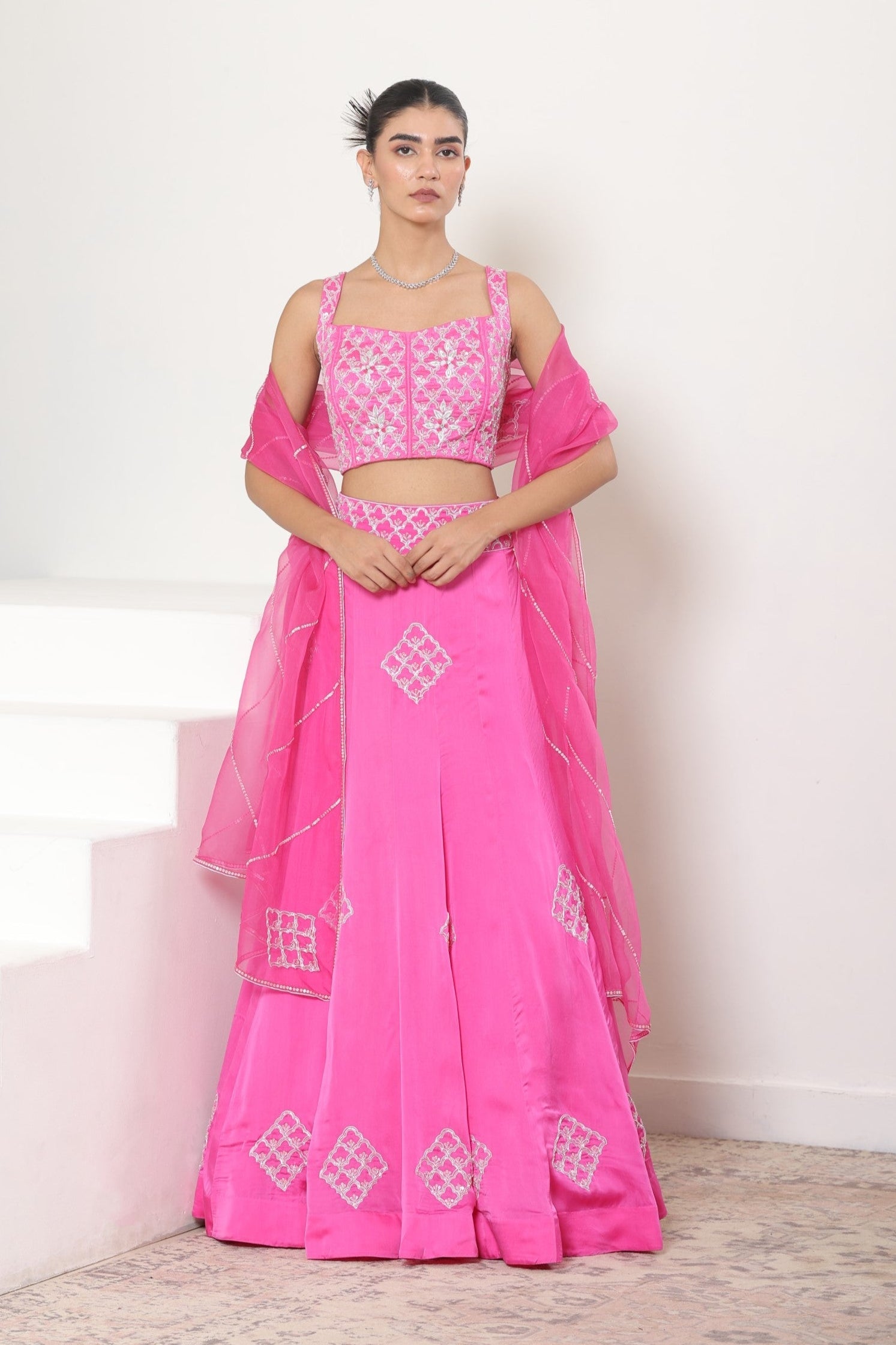 Woman wearing a pink traditional outfit with white embroidery on a light background; Pink satin organza lehenga, embroidered designer outfit, premium reception wear, elegant festive attire, traditional bridal ensemble, Sunanta Madaan, Boho Indo-Western dress, Indo-Western fusion wear, Indo-Western attire for engagement, Indo-Western outfit for sangeet, Indo-Western draped dress, Indo-Western embroidered skirt, Indo-Western embroidered dress, near me, Mumbai, Delhi, Hyderabad, Bangalore, Pune
