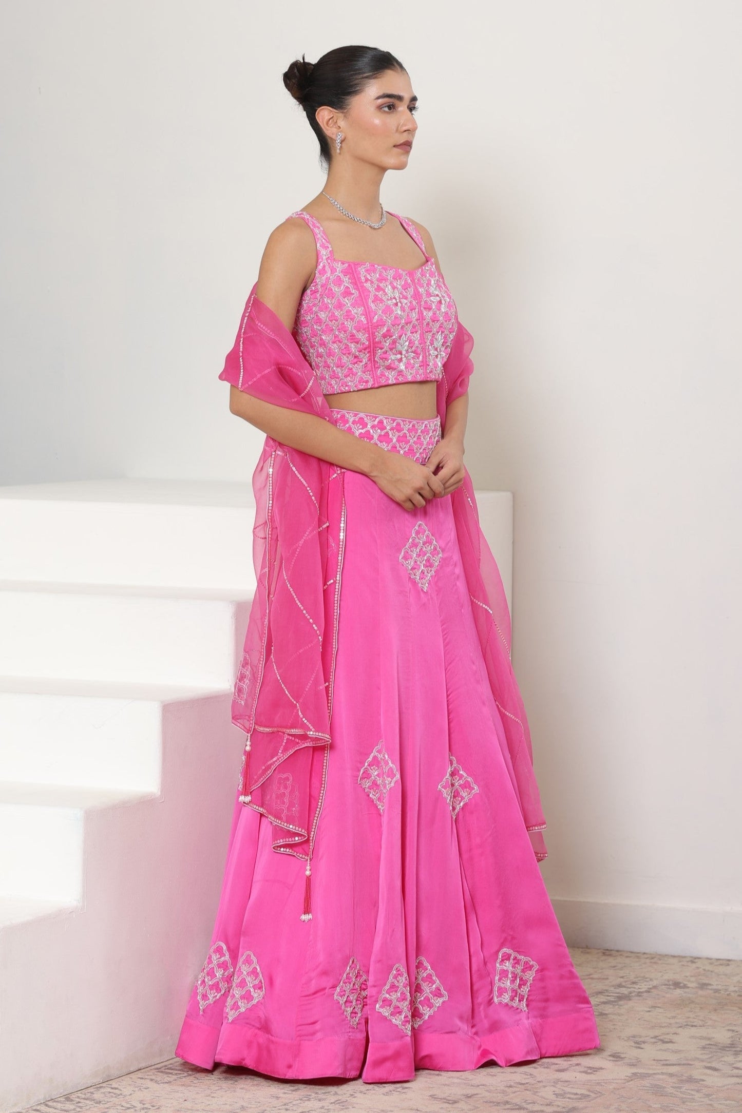 Woman wearing a pink traditional outfit with white patterns on a white background; Pink satin organza lehenga, embroidered designer outfit, premium reception wear, elegant festive attire, traditional bridal ensemble, Sunanta Madaan, Boho Indo-Western dress, Indo-Western fusion wear, Indo-Western attire for engagement, Indo-Western outfit for sangeet, Indo-Western draped dress, Indo-Western embroidered skirt, Indo-Western embroidered dress, near me, Mumbai, Delhi, Hyderabad, Bangalore, Pune