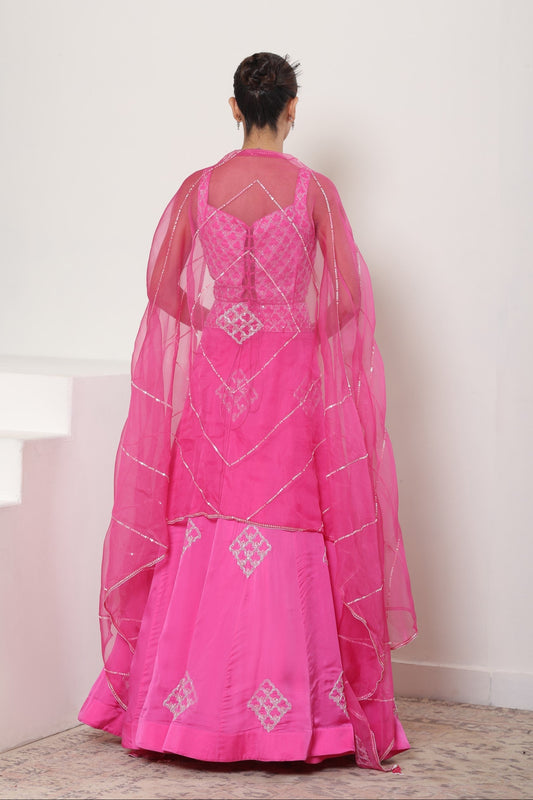 Person wearing a pink traditional outfit with white embroidery in a minimalistic setting. Pink satin organza lehenga, embroidered designer outfit, premium reception wear, elegant festive attire, traditional bridal ensemble, Sunanta Madaan, Boho Indo-Western dress, Indo-Western fusion wear, Indo-Western attire for engagement, Indo-Western outfit for sangeet, Indo-Western draped dress, Indo-Western embroidered skirt, Indo-Western embroidered dress, near me, Mumbai, Delhi, Hyderabad, Bangalore, Pune