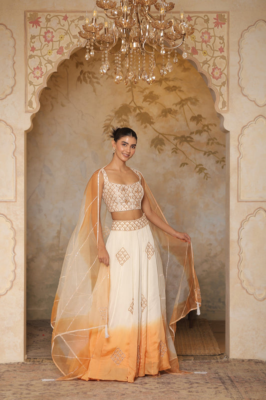Woman in a traditional outfit with a decorative background. Sunanta Madaan – Ivory-Orange Satin Organza Lehenga, Embroidered Designer Outfit, Elegant Festive Attire, Premium Party & Reception Wear, Boho Indo-Western Dress, Indo-Western Fusion Wear, Indo-Western Attire for Engagement, Indo-Western Outfit for Sangeet, Indo-Western Draped & Embroidered Skirt, Mumbai, Delhi, Hyderabad, Bangalore, Pune, near me