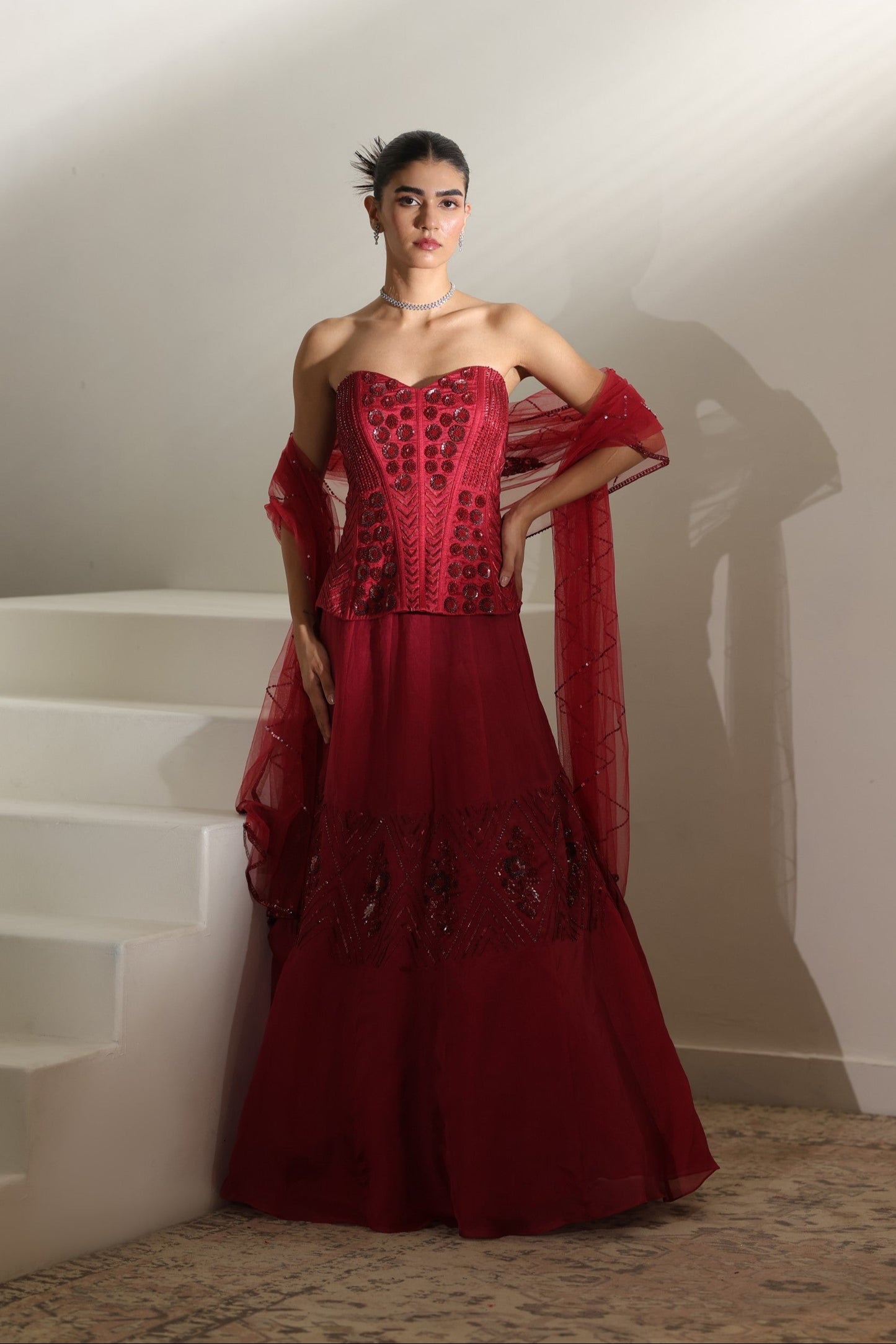 Woman wearing a red evening gown with a plain background; Sunanta Madaan – Burgundy Raw Silk & Organza Embroidered Lehenga, Elegant Bridal Wear, Premium Festive Outfit, Boho Indo-Western Dress, Indo-Western Fusion Wear, Indo-Western Attire for Engagement, Indo-Western Outfit for Sangeet, Indo-Western Draped & Embroidered Skirt, Women’s Designer Bridal Ensemble, Delhi, Jaipur, Hyderabad, Ahmedabad, Bangalore, near me