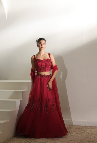 Woman wearing a red traditional outfit with intricate designs in a minimal indoor setting. Sunanta Madaan – Burgundy Organza Hand-Embroidered Lehenga, Elegant Wedding Wear, Premium Festive Outfit, Boho Indo-Western Dress, Indo-Western Fusion Wear, Indo-Western Attire for Engagement, Indo-Western Outfit for Sangeet, Indo-Western Draped & Embroidered Skirt, Women’s Designer Bridal Ensemble, Mumbai, Jaipur, Hyderabad, Ahmedabad, Pune, near me