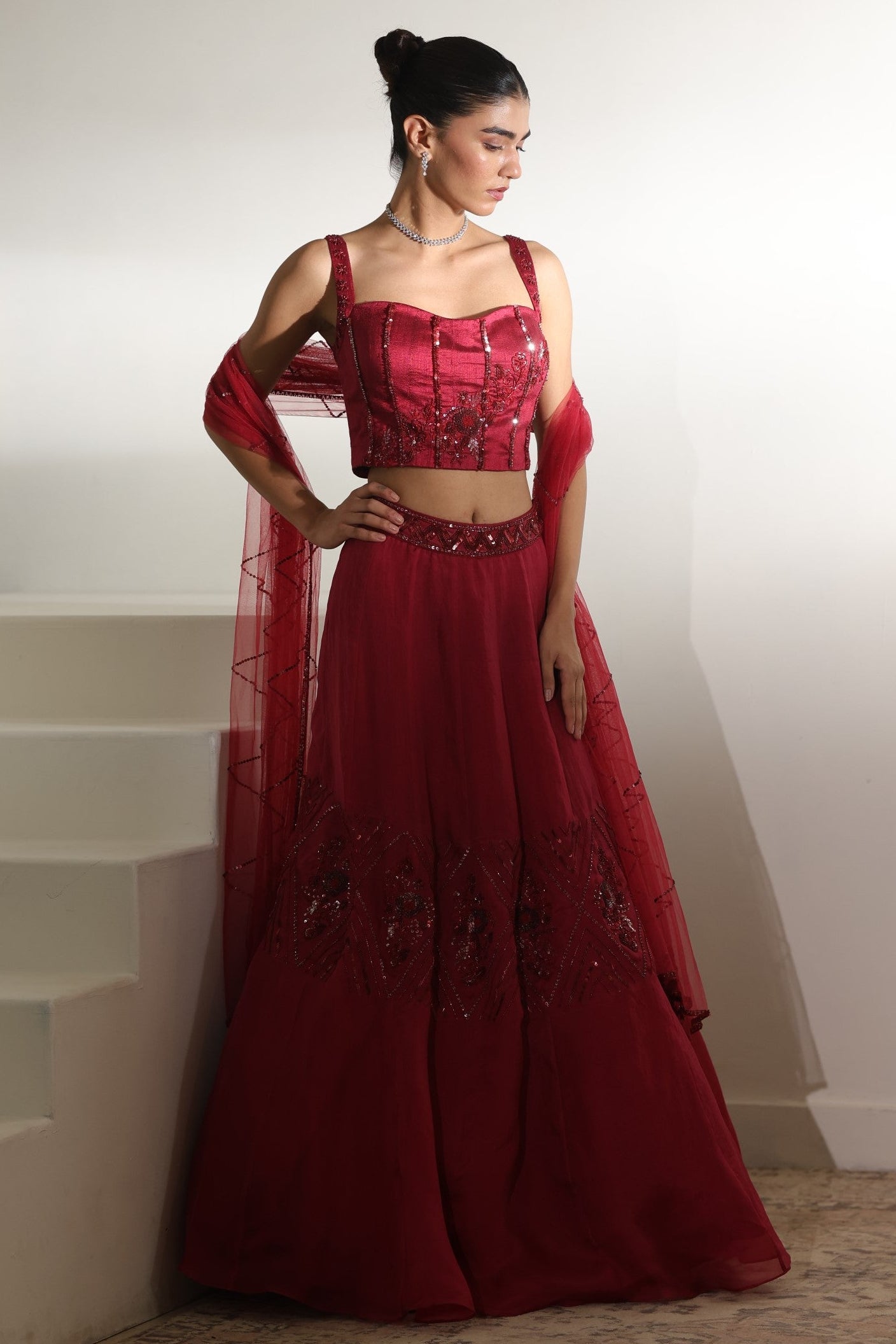 Woman in a red traditional outfit standing in a minimalistic setting; Sunanta Madaan – Burgundy Organza Hand-Embroidered Lehenga, Elegant Wedding Wear, Premium Festive Outfit, Boho Indo-Western Dress, Indo-Western Fusion Wear, Indo-Western Attire for Engagement, Indo-Western Outfit for Sangeet, Indo-Western Draped & Embroidered Skirt, Women’s Designer Bridal Ensemble, Mumbai, Jaipur, Hyderabad, Ahmedabad, Pune, near me