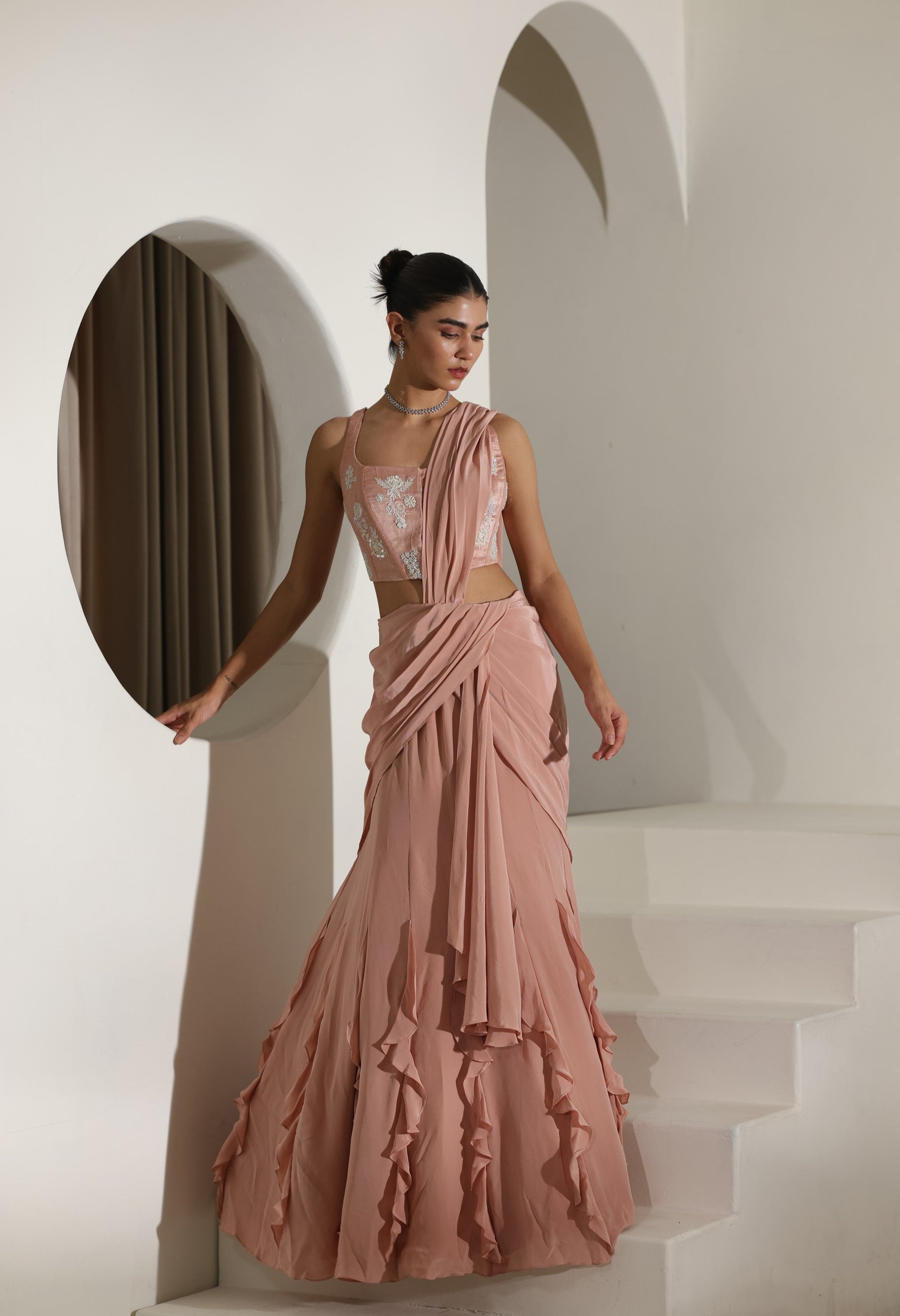 Woman in a pink gown standing in a white architectural setting; Sunanta Madaan – Mocha Mousse Crepe Embroidered Drape Lehenga Saree, Premium Festive Wear, Elegant Party Outfit, Boho Indo-Western Dress, Indo-Western Fusion Wear, Indo-Western Attire for Engagement, Indo-Western Outfit for Sangeet, Indo-Western Draped & Embroidered Skirt, Women’s Designer Festive Ensemble, Delhi, Jaipur, Hyderabad, Ahmedabad, Bangalore, near me