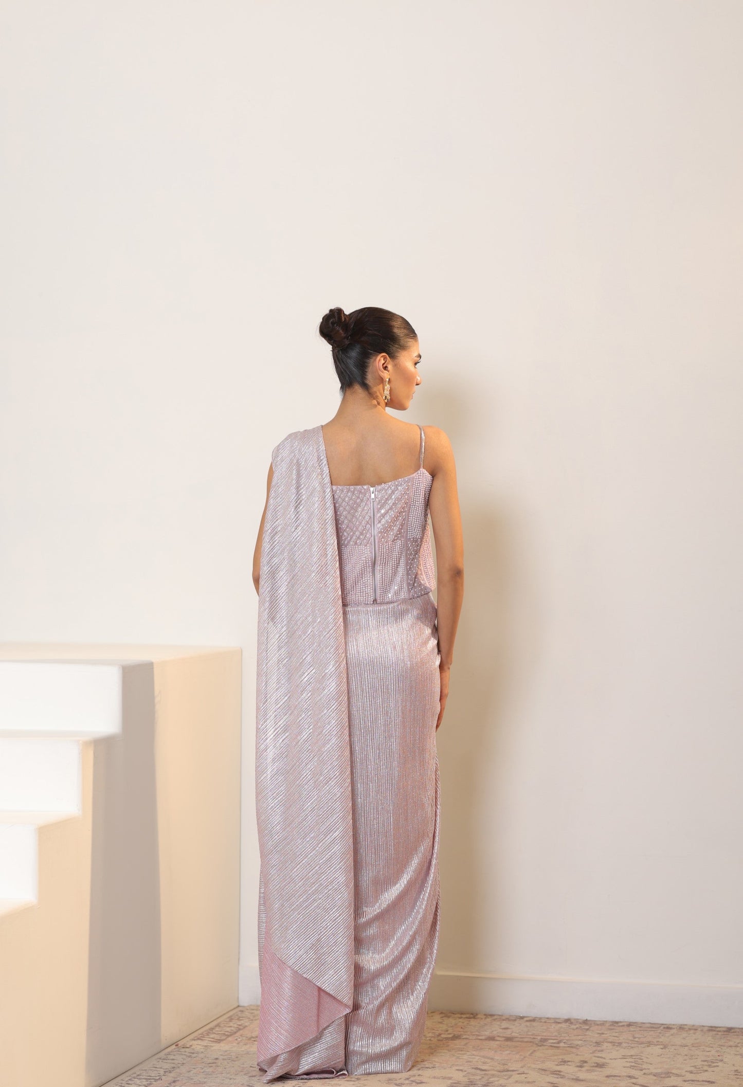 Woman wearing a light pink saree with a white background; simple saree, latest saree design, sarees online, pink saree, satin saree, ready made saree, lite colour saree, fancy saree, lycra saree, Sunantamadaan Saree, pre draped saree, peach saree, simple saree, latest saree design, sarees online, pink saree, satin saree, ready made saree, white colour saree, fancy saree, party wear saree, Sunanta Madaan – Pink Metallic Lycra Crepe Saree, Premium Reception Wear, Elegant Party Outfit, Boho Indo-Western Dress,
