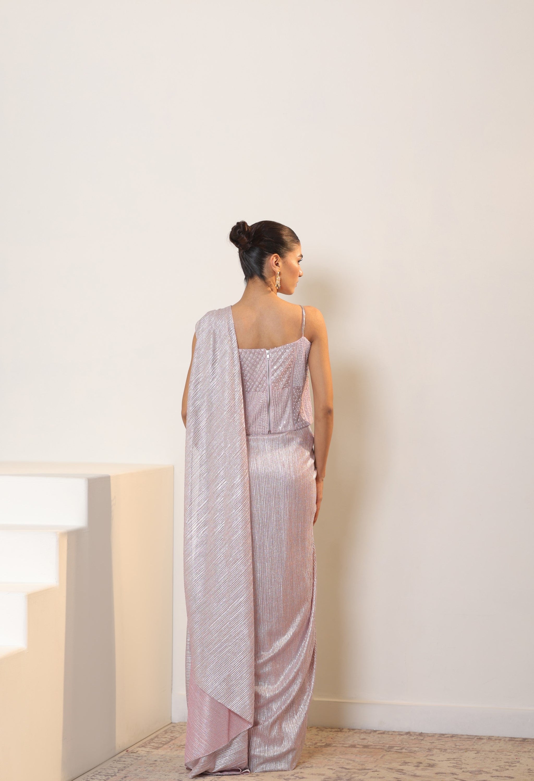 Woman wearing a light pink saree with a white background; simple saree, latest saree design, sarees online, pink saree, satin saree, ready made saree, lite colour saree, fancy saree, lycra saree, Sunantamadaan Saree, pre draped saree, peach saree, simple saree, latest saree design, sarees online, pink saree, satin saree, ready made saree, white colour saree, fancy saree, party wear saree, Sunanta Madaan – Pink Metallic Lycra Crepe Saree, Premium Reception Wear, Elegant Party Outfit, Boho Indo-Western Dress,