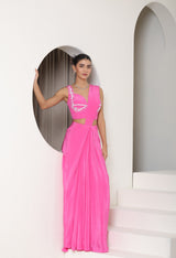 Woman wearing a bright pink dress with cut-out design in a minimalistic setting. Pink crepe saree, embroidered cocktail saree, premium party wear saree, designer festive outfit, elegant evening saree, Sunanta Madaan