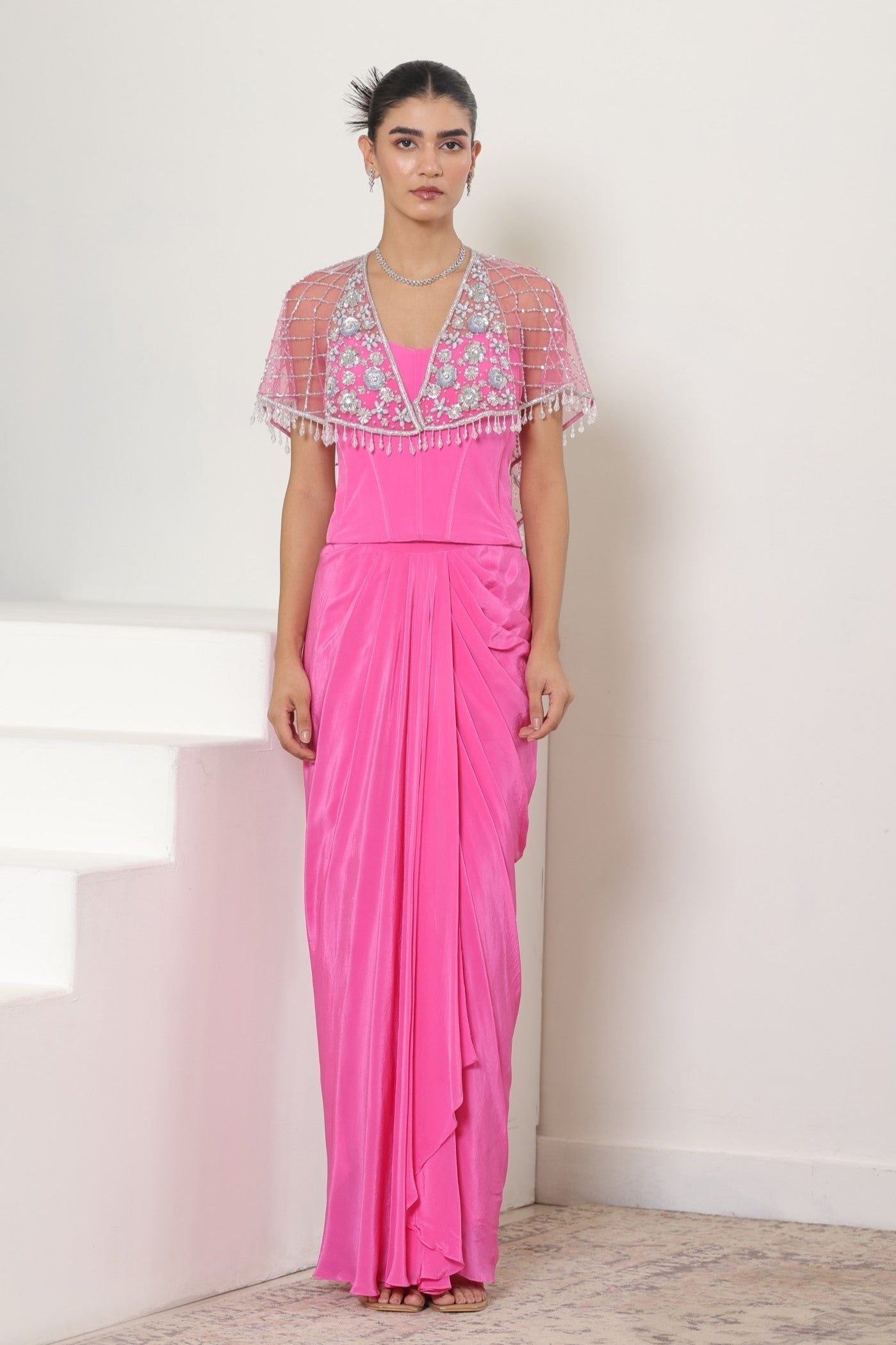 Woman wearing a pink dress with an embroidered top against a white background; Pink crepe skirt set, embroidered cape outfit, handcrafted engagement wear, elegant festive ensemble, designer ethnic attire, Sunanta Madaan