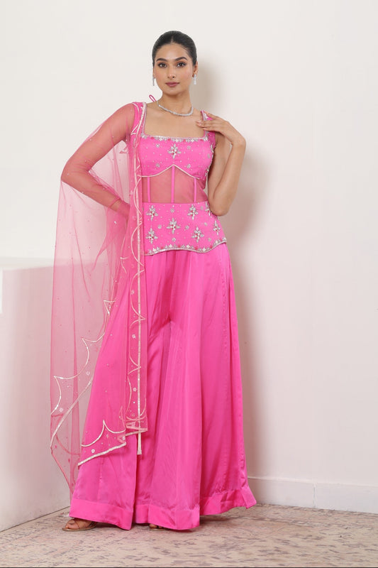 Woman wearing a pink traditional outfit with a white embroidered border on a white background; Pink satin organza sharara, embroidered festive outfit, elegant occasional wear, designer ethnic attire, premium traditional set, Sunanta Madaan, near me, Mumbai, Delhi, Hyderabad, Bangalore, Pune