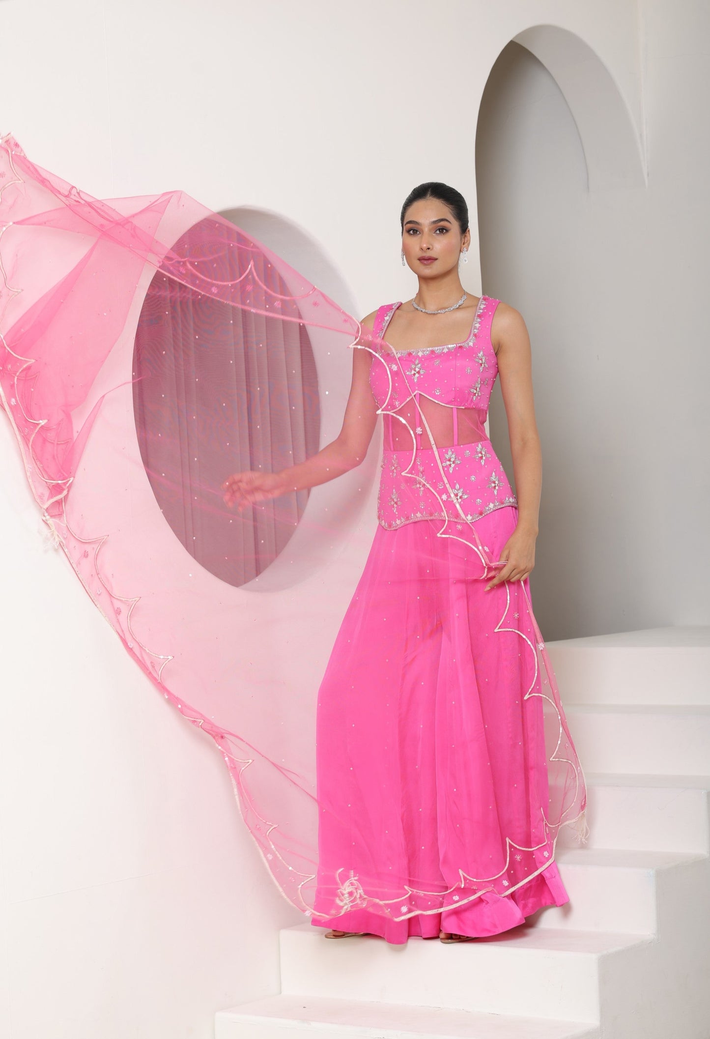 Woman in a pink traditional outfit with a sheer dupatta against a white background; Pink satin organza sharara, embroidered festive outfit, elegant occasional wear, designer ethnic attire, premium traditional set, Sunanta Madaan, near me, Mumbai, Delhi, Hyderabad, Bangalore, Pune