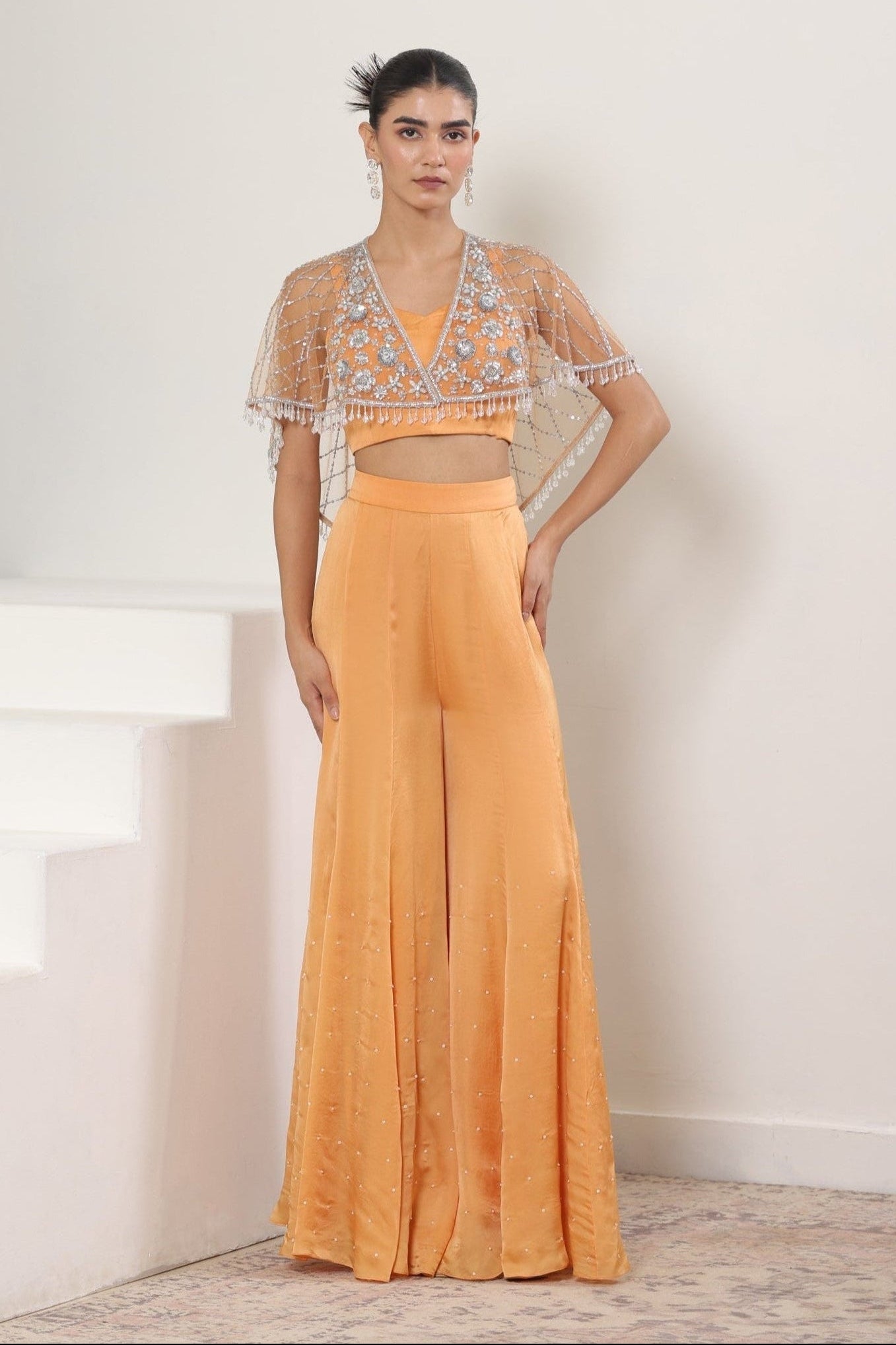 Woman wearing an orange outfit with a sheer top against a white background; Orange satin organza sharara, embroidered cape set, festive ethnic outfit, elegant designer wear, premium traditional attire, Sunanta Madaan, near me, Mumbai, Delhi, Hyderabad, Bangalore, Pune