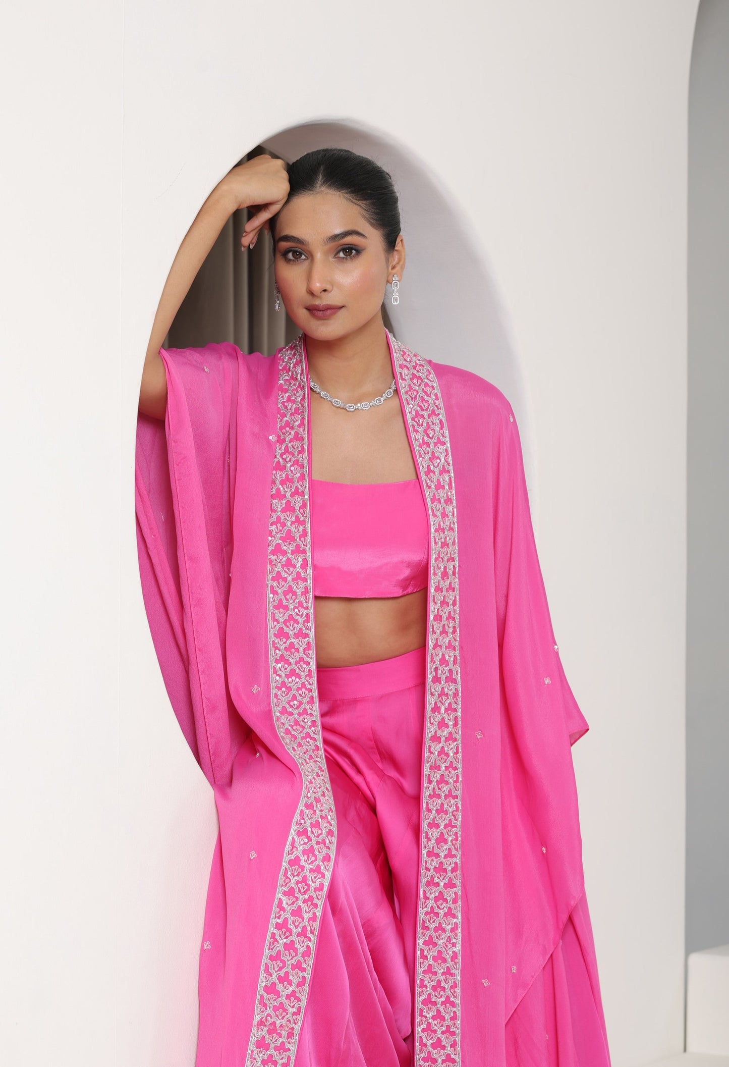 Woman wearing a pink traditional outfit with a white border against a white background; Hot pink sharara set, embroidered crepe outfit, handcrafted evening wear, elegant festive attire, designer party ensemble, Sunanta Madaan