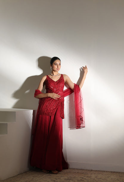 Woman in a red saree standing against a white wall; Sunanta Madaan – Burgundy Satin Organza Sharara with Embroidered Corset, Wedding Wear, Elegant Festive Outfit, Boho Indo-Western Dress, Indo-Western Fusion Wear, Indo-Western Attire for Engagement, Indo-Western Outfit for Sangeet, Indo-Western Draped & Embroidered Skirt, Women’s Designer Party Wear, Delhi, Jodhpur, Hyderabad, Ahmedabad, Bangalore, near me