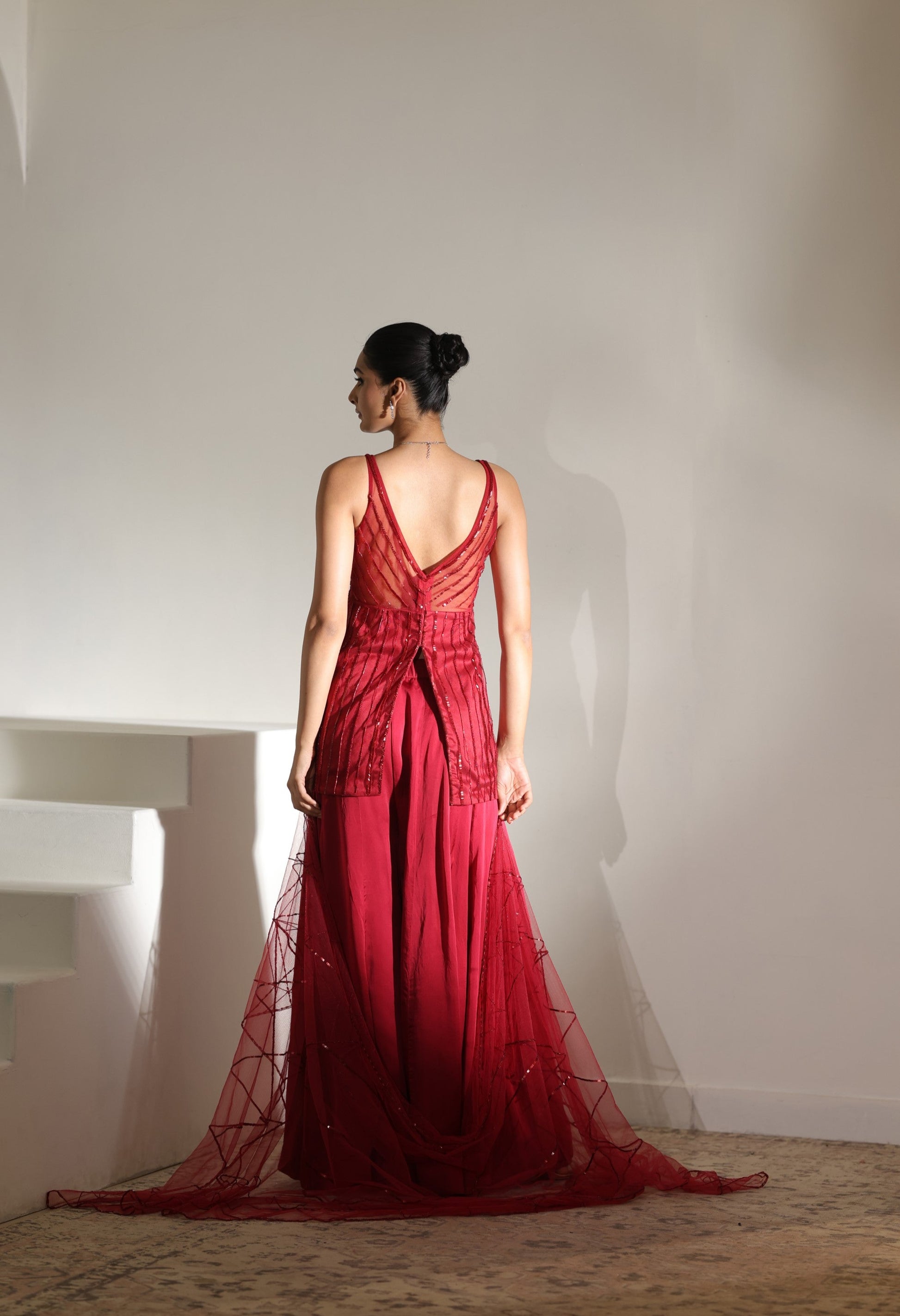 Woman in a red evening gown standing against a plain wall. Sunanta Madaan – Burgundy Satin Organza Sharara with Embroidered Corset, Wedding Wear, Elegant Festive Outfit, Boho Indo-Western Dress, Indo-Western Fusion Wear, Indo-Western Attire for Engagement, Indo-Western Outfit for Sangeet, Indo-Western Draped & Embroidered Skirt, Women’s Designer Party Wear, Delhi, Jodhpur, Hyderabad, Ahmedabad, Bangalore, near me
