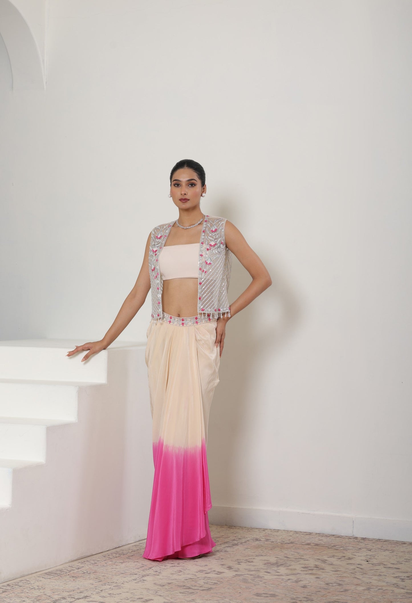 Woman wearing a traditional outfit with a white and pink gradient dress against a white wall. Ivory pink skirt dress, viscose crepe outfit, pre-draped designer wear, premium occasion attire, elegant festive ensemble, Sunanta Madaan, near me, Mumbai, Delhi, Hyderabad, Bangalore, Pune