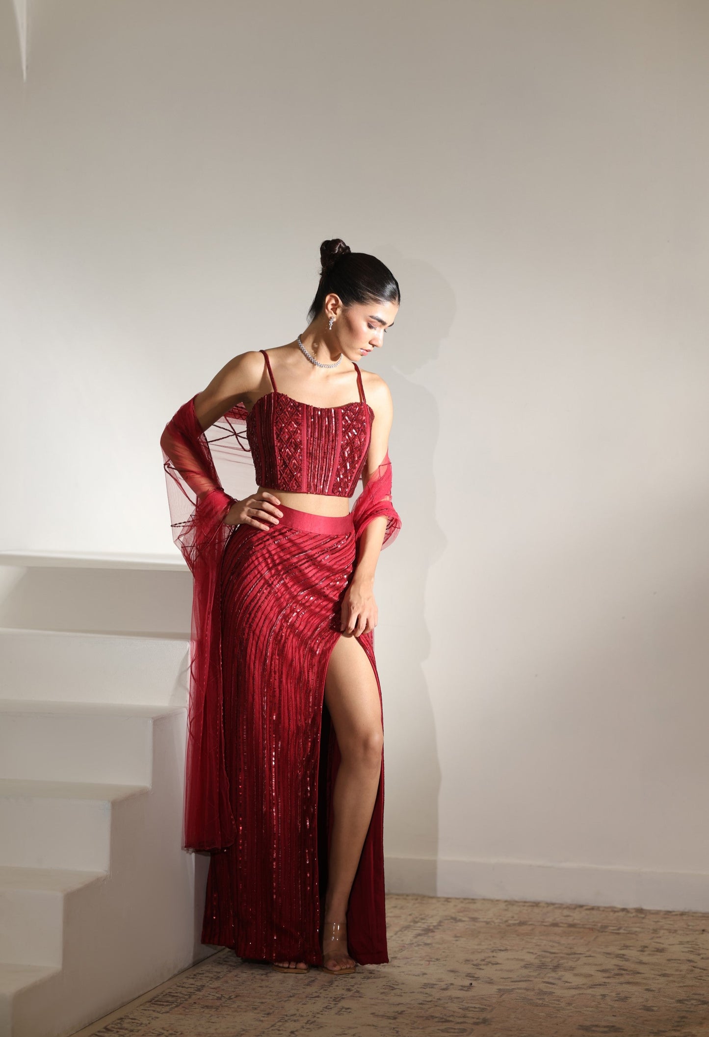 Woman in a red evening gown standing against a plain wall. Sunanta Madaan – Burgundy Satin Embroidered Western Skirt Set, Handcrafted Festive Wear, Elegant Party Outfit, Boho Indo-Western Dress, Indo-Western Fusion Wear, Indo-Western Attire for Engagement, Indo-Western Outfit for Sangeet, Indo-Western Draped & Embroidered Skirt, Women’s Designer Festive Ensemble, Mumbai, Jaipur, Hyderabad, Ahmedabad, Pune, near me