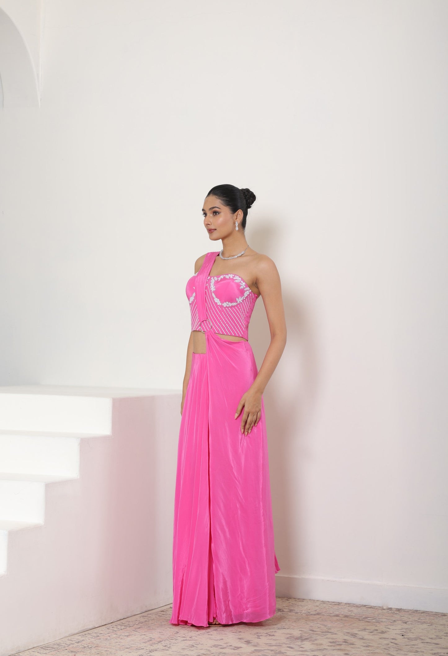 Woman in a pink dress standing against a white wall; Hot pink crepe saree, hand embroidered saree, premium cocktail outfit, elegant evening wear, designer festive saree, Sunanta Madaan