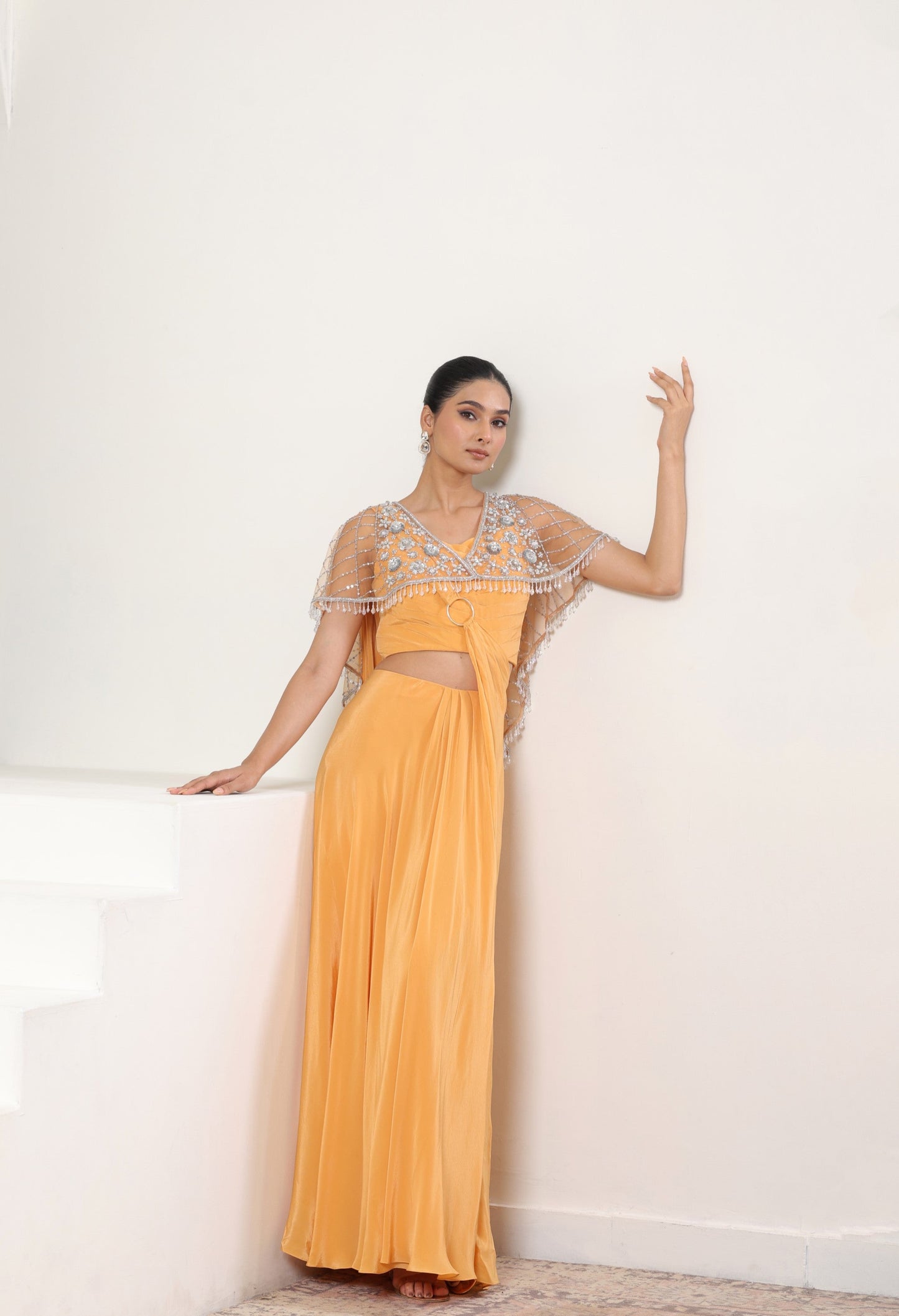 Woman wearing a yellow evening saree with intricate detailing on cape; elegant festive outfit, premium evening wear, Sunanta Madaan, Orange crepe saree, embroidered cape saree, designer reception saree