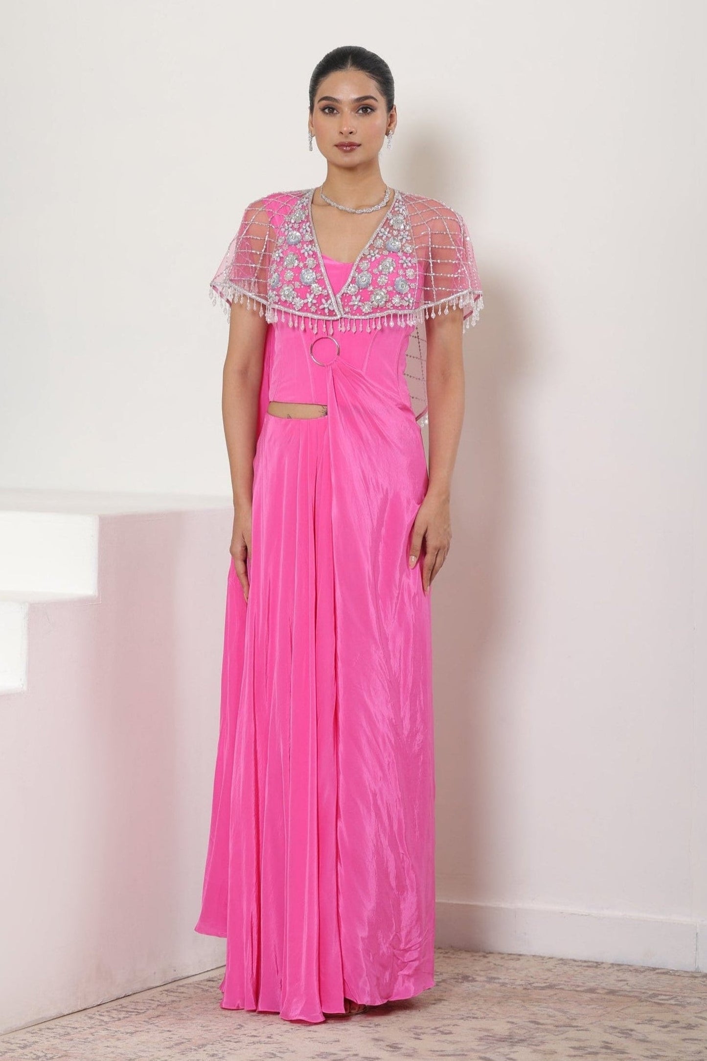 Woman wearing a pink evening gown with a white embroidered top against a white background; Pink crepe saree, embroidered cape saree, designer wedding saree, elegant bridal wear, festive ethnic outfit, Sunanta Madaan