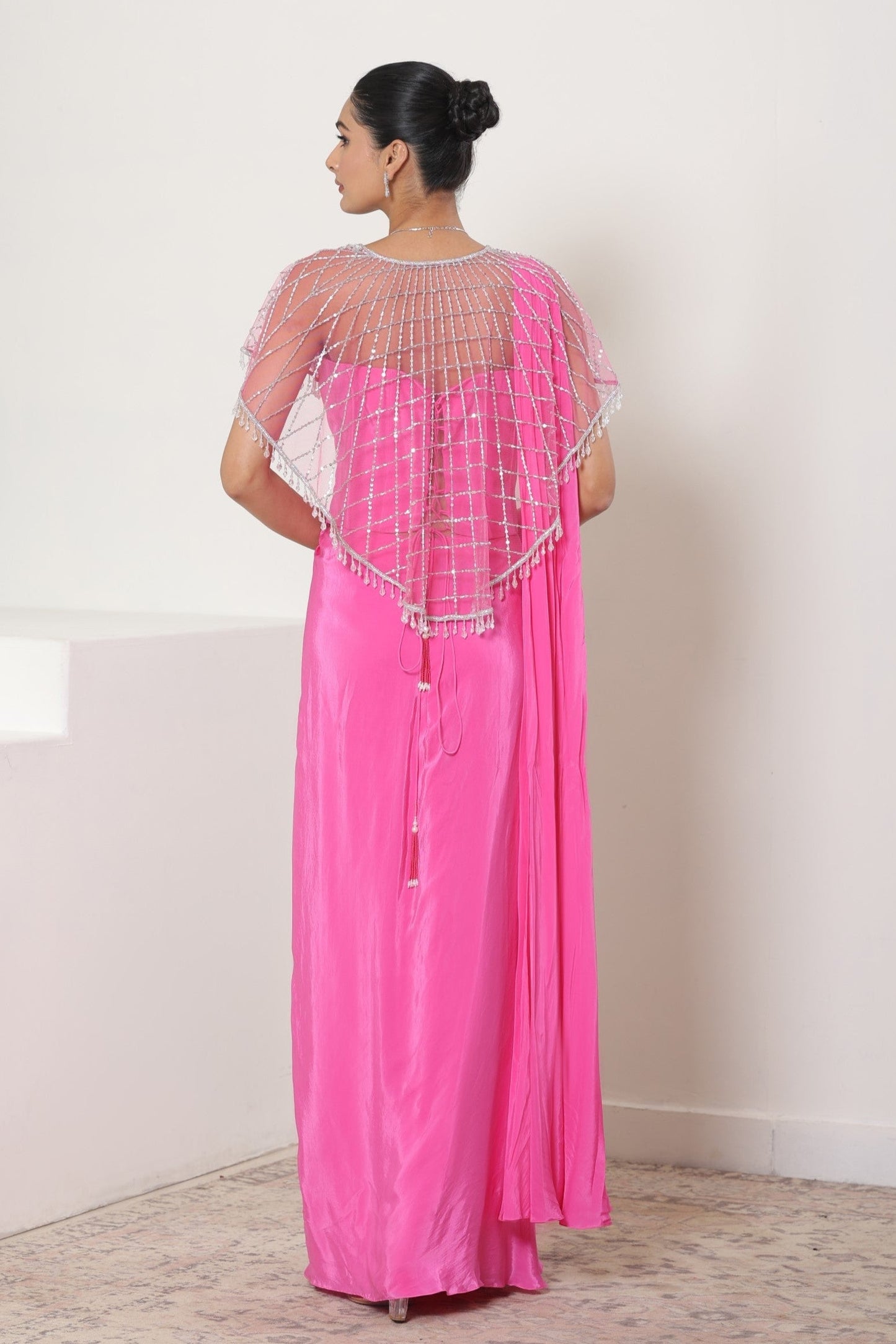 Woman wearing a pink outfit with a sheer overlay against a white background; designer wedding saree, Pink crepe saree, embroidered cape saree, elegant bridal wear, festive ethnic outfit, Sunanta Madaan