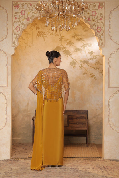 Woman in a mustard yellow dress with intricate detailing standing in a decorated room. Golden yellow crepe saree, designer cape saree, premium haldi outfit, elegant festive wear, embroidered ethnic saree, Sunanta Madaan
