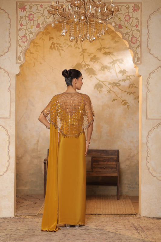 Woman in a mustard yellow dress with intricate detailing standing in a decorated room. Golden yellow crepe saree, designer cape saree, premium haldi outfit, elegant festive wear, embroidered ethnic saree, Sunanta Madaan