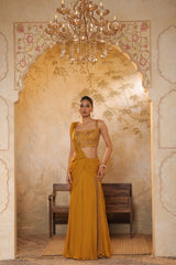 Woman in a mustard yellow saree by Sunanta Madaan standing in an ornate room with a chandelier. Golden yellow saree, chiffon embroidered saree, elegant traditional saree, festive ethnic wear, designer saree online, Sunanta Madaan