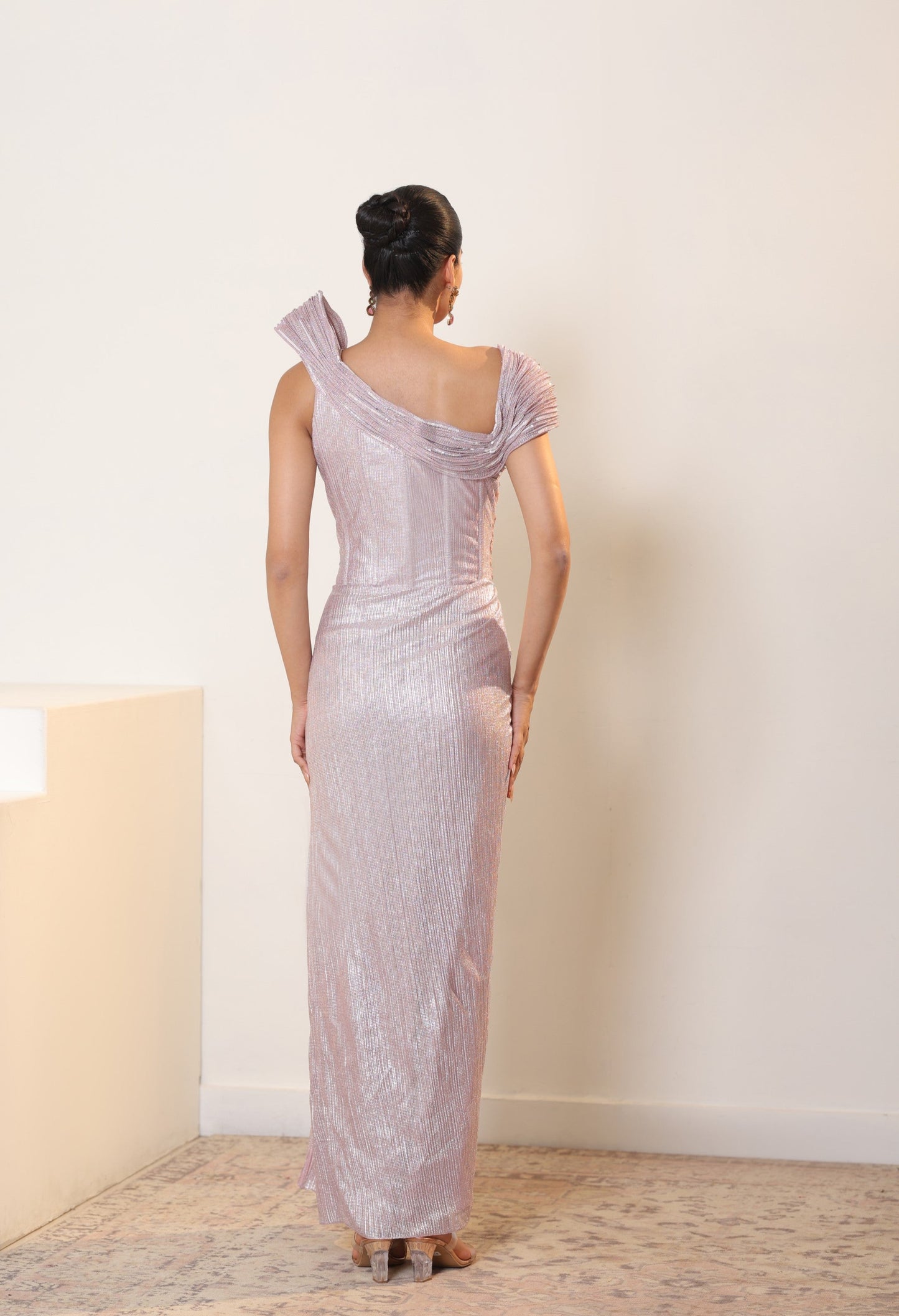 Woman wearing a one-shoulder evening gown in a minimal indoor setting; Sunanta Madaan – Pink Metallic Lycra Crepe Embroidered Gown, Elegant Designer Wear, Evening Party Dress, Boho Indo-Western Dress, Indo-Western Fusion Wear, Women’s Formal Gown, Indo-Western Outfit for Reception, Party Outfit, Indo-Western Draped Dress, Mumbai, Jaipur, Bangalore, Ahmedabad, Pune, near me