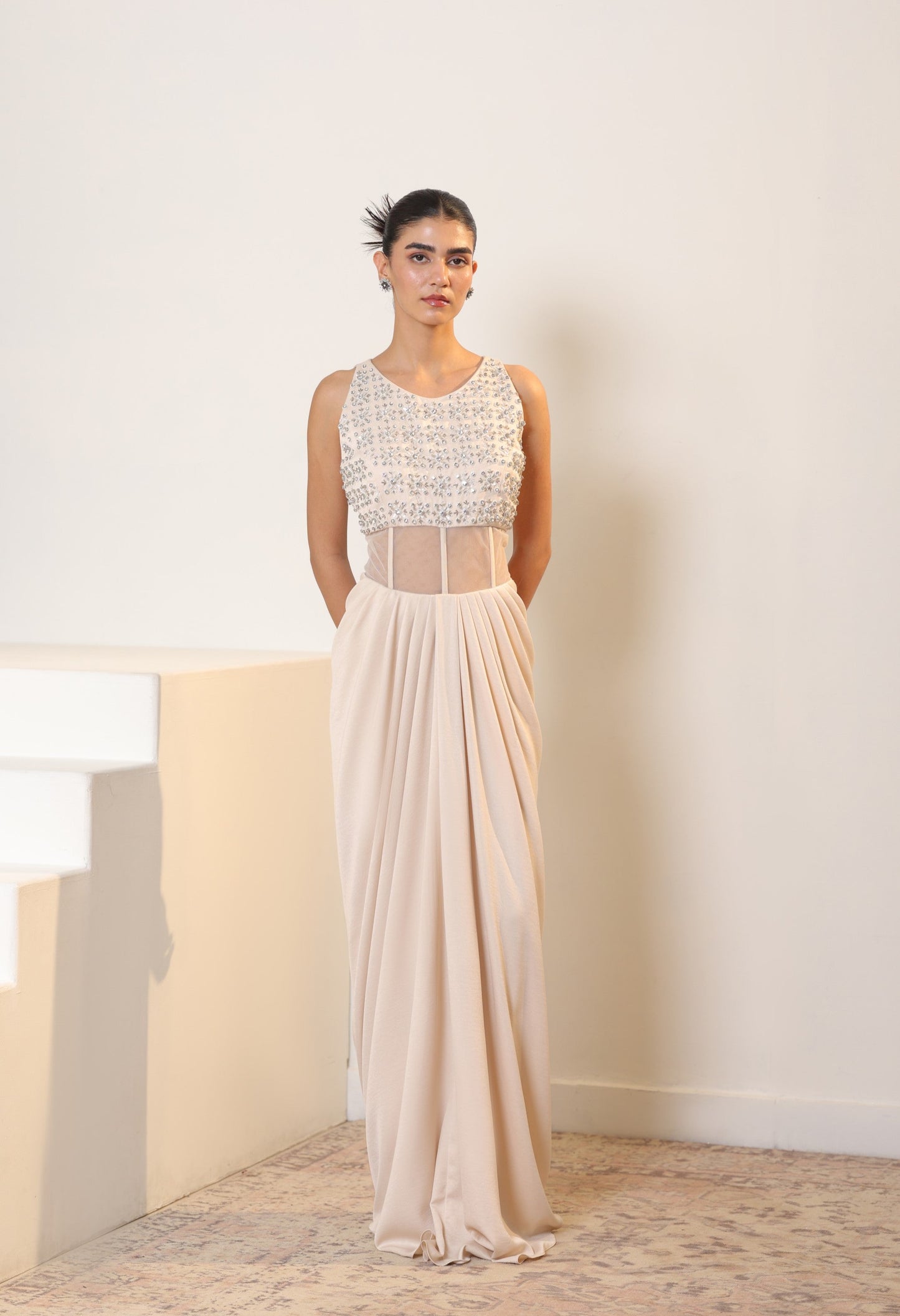 Woman wearing a long, elegant dress with a white top and sheer skirt against a neutral background. Sunanta Madaan – Ivory Crepe Satin Western Embroidered Gown, Premium Cocktail Wear, Elegant Party Outfit, Boho Indo-Western Dress, Indo-Western Fusion Wear, Women’s Formal Evening Dress, Indo-Western Outfit for Reception, Party Outfit, Indo-Western Draped Dress, Jaipur, Delhi, Hyderabad, Ahmedabad, Bangalore, near me