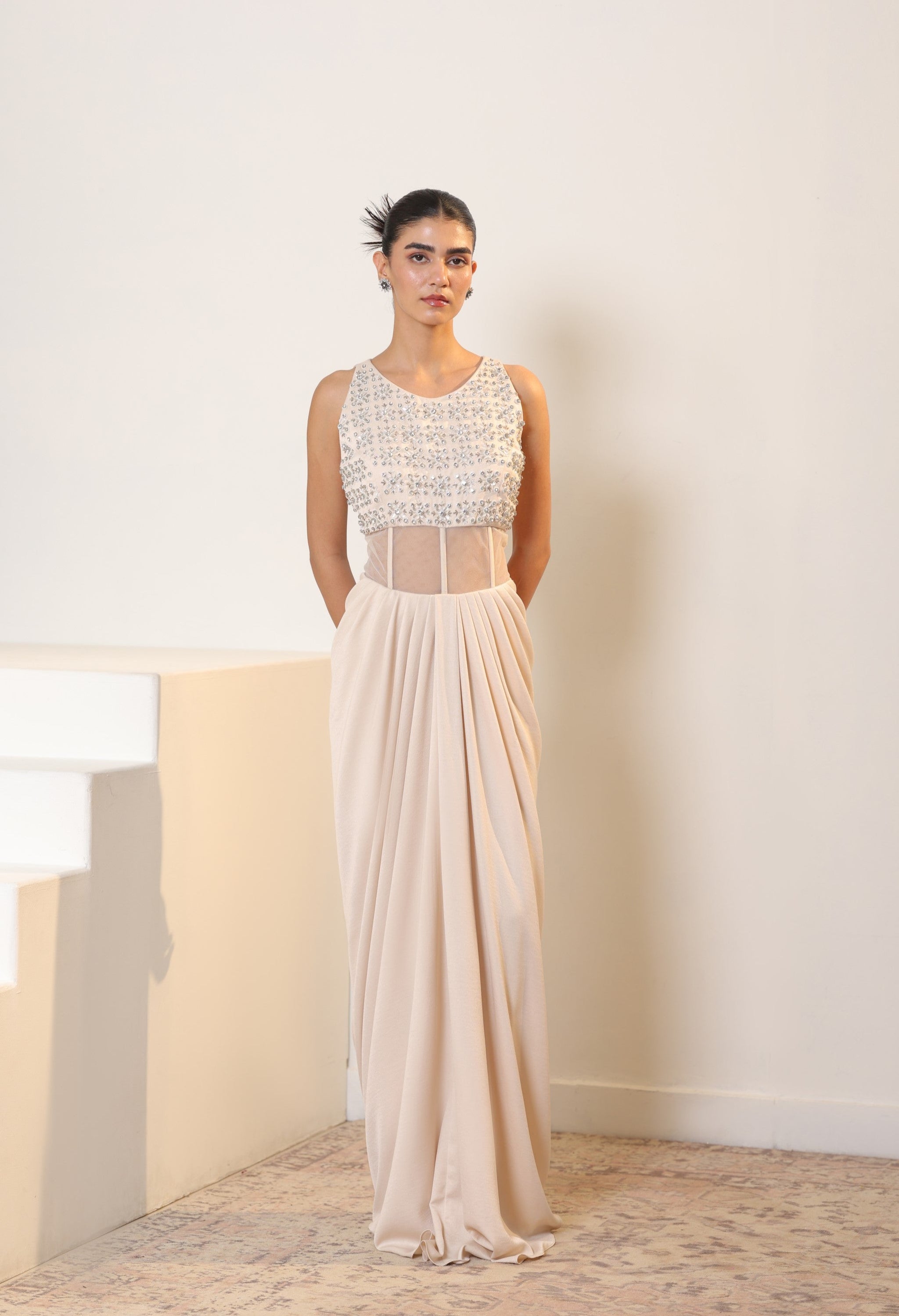 Woman wearing a long, elegant dress with a white top and sheer skirt against a neutral background. Sunanta Madaan – Ivory Crepe Satin Western Embroidered Gown, Premium Cocktail Wear, Elegant Party Outfit, Boho Indo-Western Dress, Indo-Western Fusion Wear, Women’s Formal Evening Dress, Indo-Western Outfit for Reception, Party Outfit, Indo-Western Draped Dress, Jaipur, Delhi, Hyderabad, Ahmedabad, Bangalore, near me