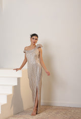 Woman in a silver one-shoulder evening gown standing on a staircase. Sunanta Madaan – Champagne Metallic Lycra Crepe Embroidered Gown, Elegant Cocktail Wear, Evening Party Dress, Boho Indo-Western Dress, Indo-Western Fusion Wear, Women’s Formal Gown, Indo-Western Outfit for Reception, Party Outfit, Indo-Western Draped Dress, Jaipur, Delhi, Pune, Ahmedabad, Hyderabad, near me