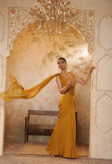 Woman in a yellow saree standing in an ornate room with a chandelier. Golden yellow saree, chiffon embroidered saree, elegant traditional saree, festive ethnic wear, designer saree online, Sunanta Madaan